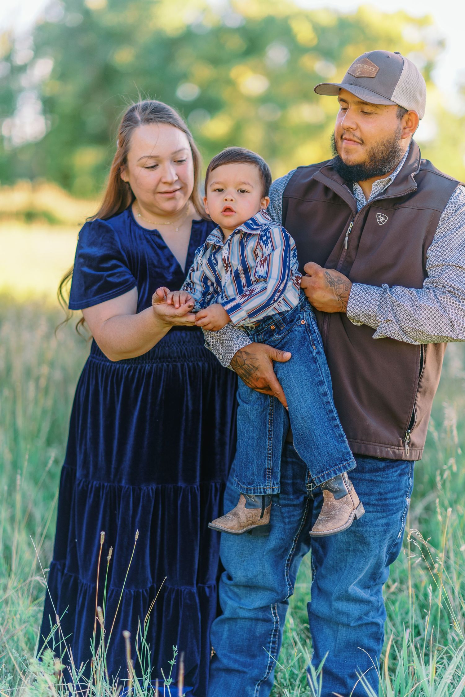 Family enjoying outdoor photo session in tall grass field wearing coordinating blue and brown outfits.