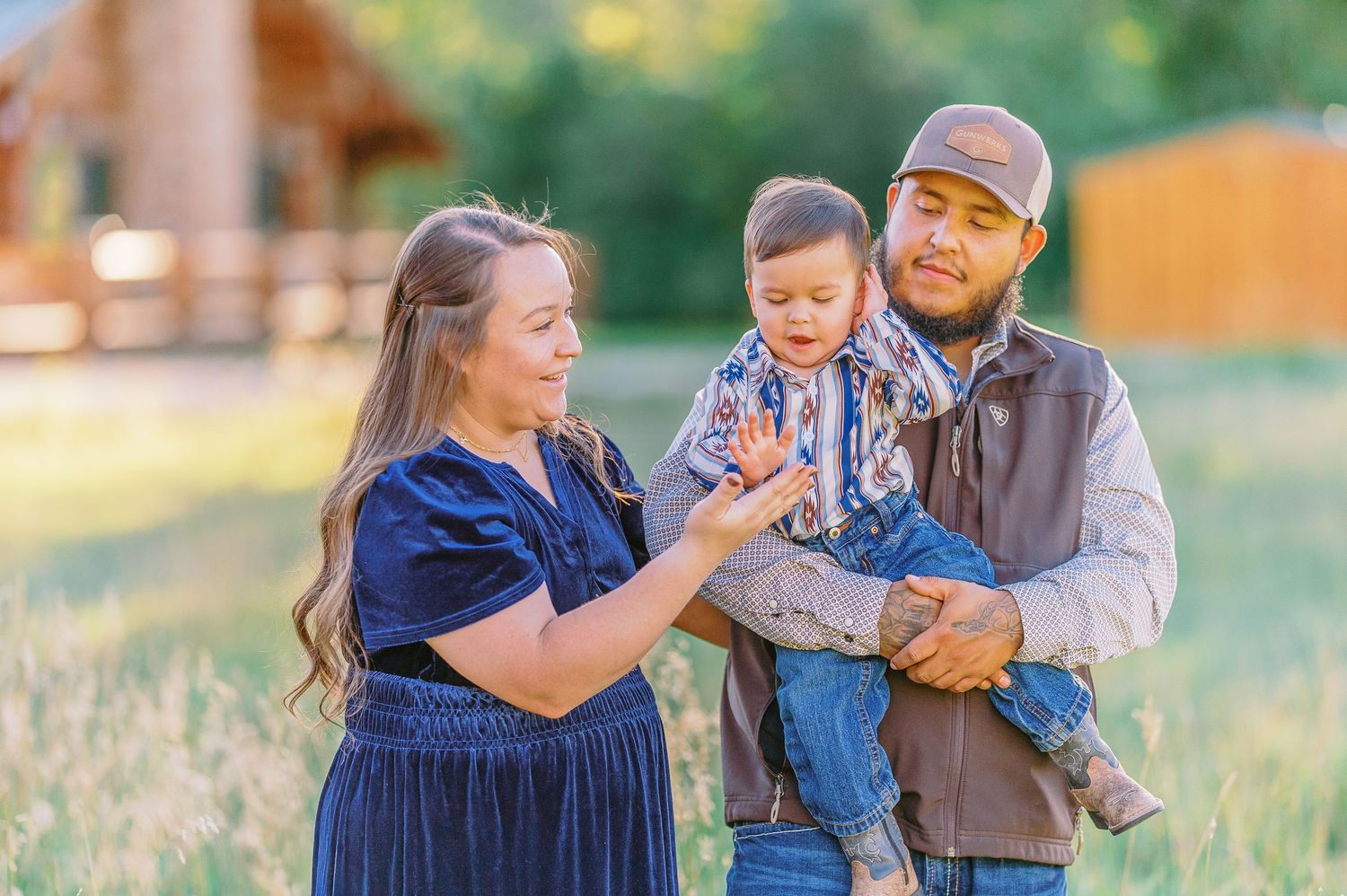 A family wearing coordinated blue and brown outfits poses together in a sunny outdoor field during golden hour.