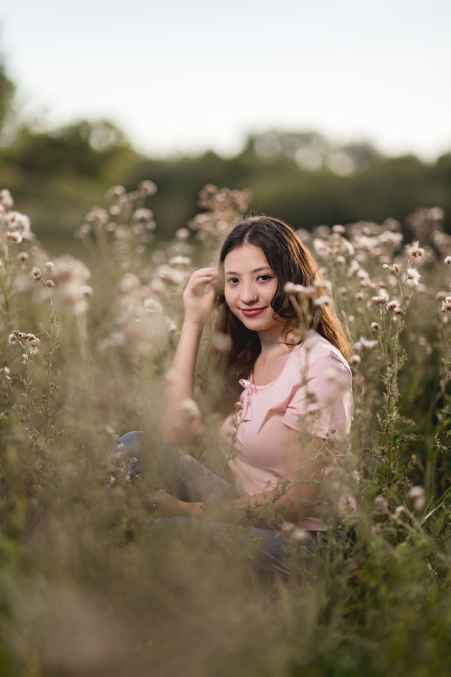 A person sits among delicate purple wildflowers in a meadow at sunset wearing a pink top.