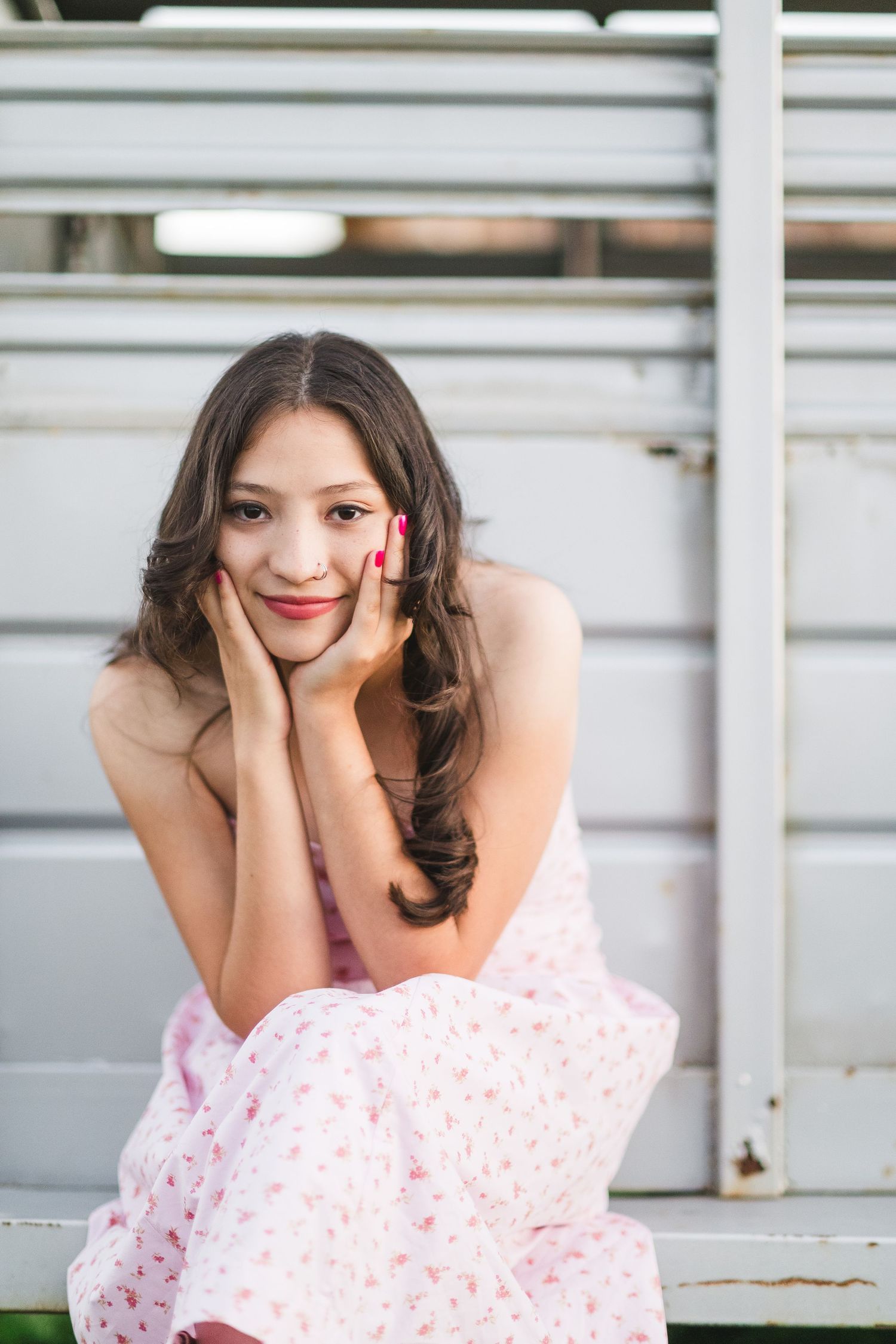Woman in pink dress poses playfully on bleachers with joyful expression during outdoor photoshoot.