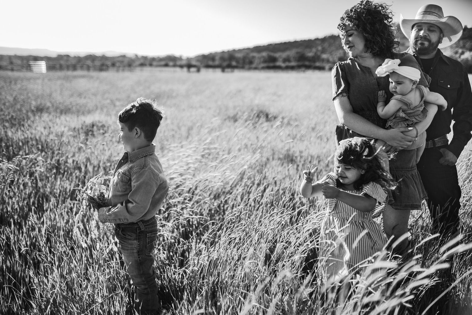 Black and white photo of a family with two young children standing in a tall grass field on a farm.
