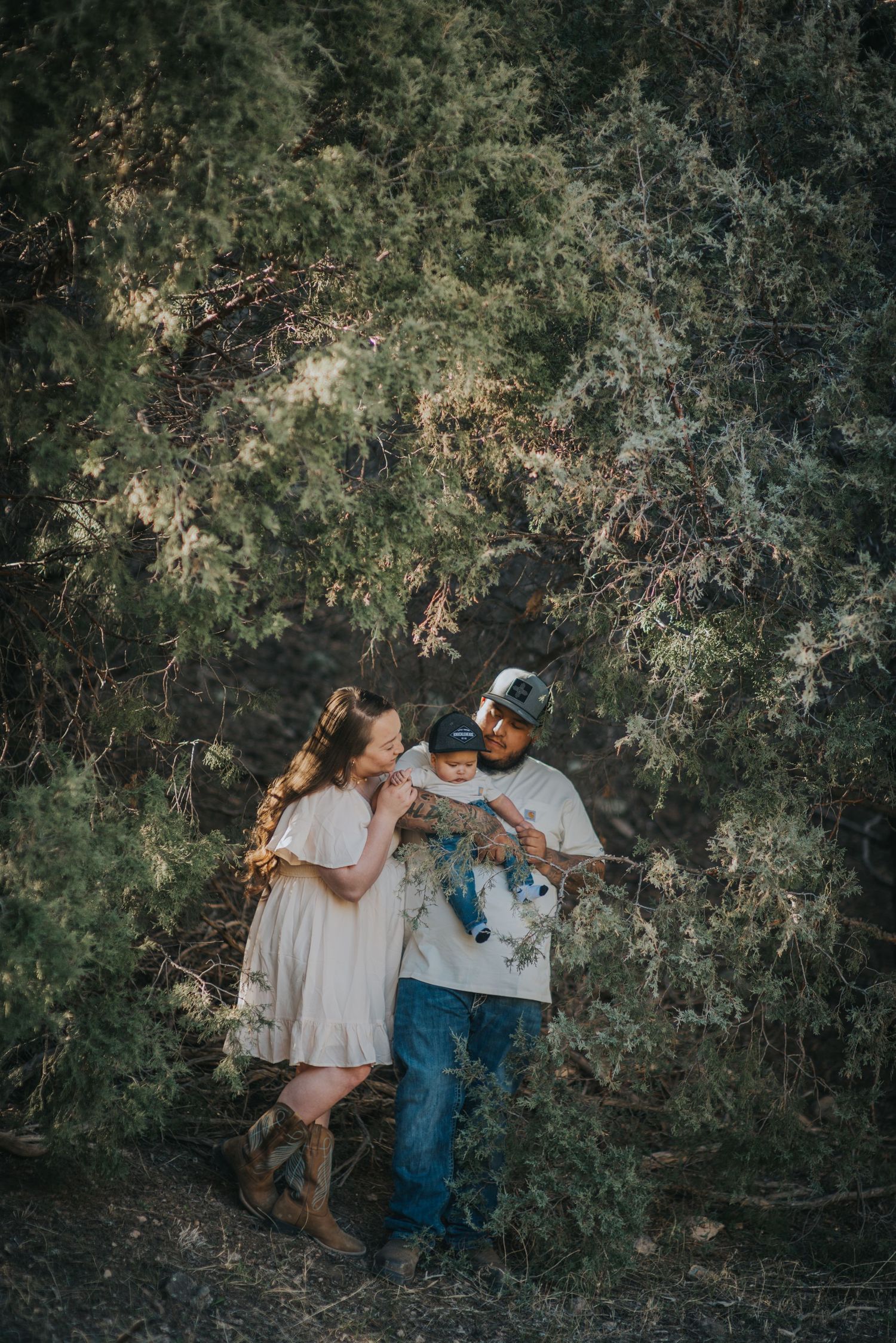 Family of three with 1-year-old son standing amidst northern New Mexico's shrubland — warm, natural light photo by Quiet Light by The Amoras