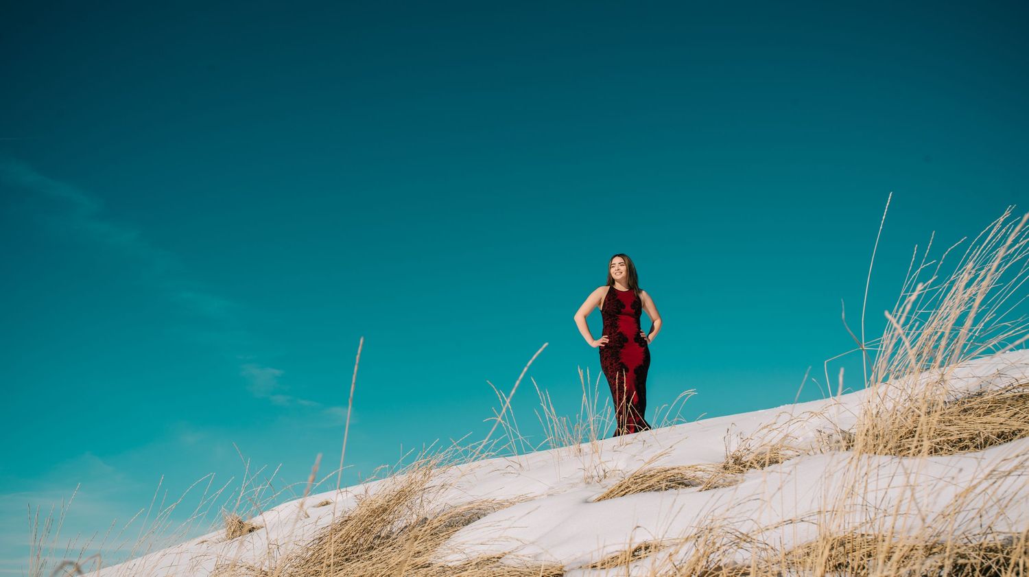 Silhouette of person standing on snowy hill against vibrant turquoise sky.