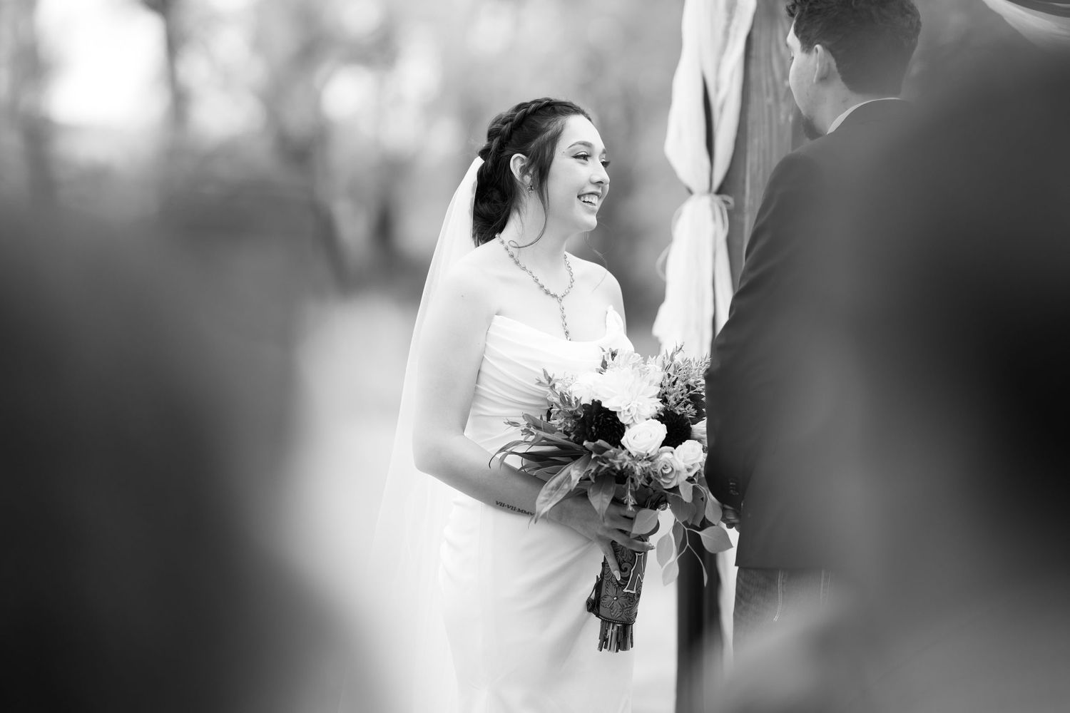 Black and white photo of a bride laughing joyfully during an outdoor wedding ceremony.
