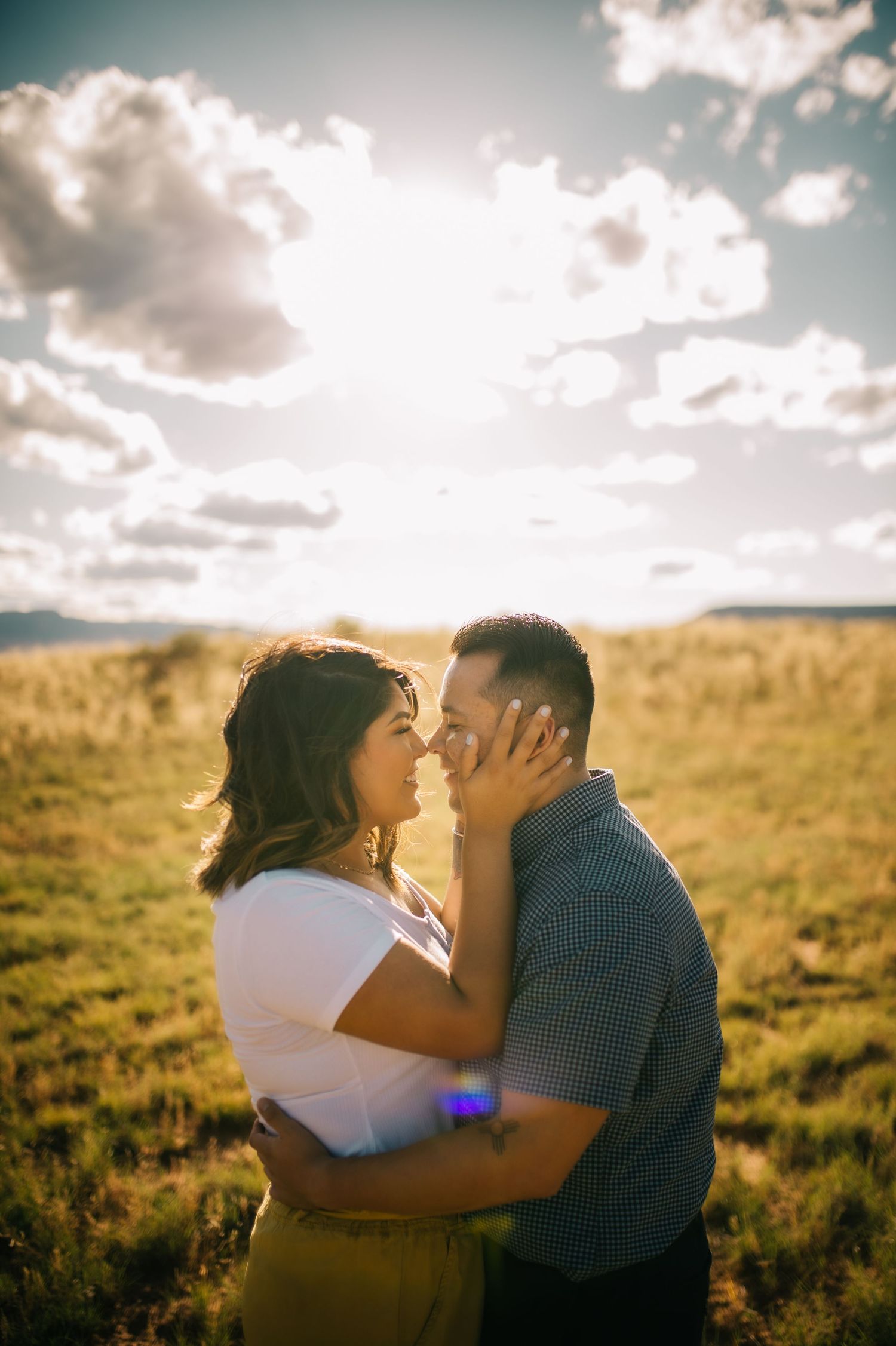 Romantic sunset engagement photo in golden field with dramatic cloudy sky.