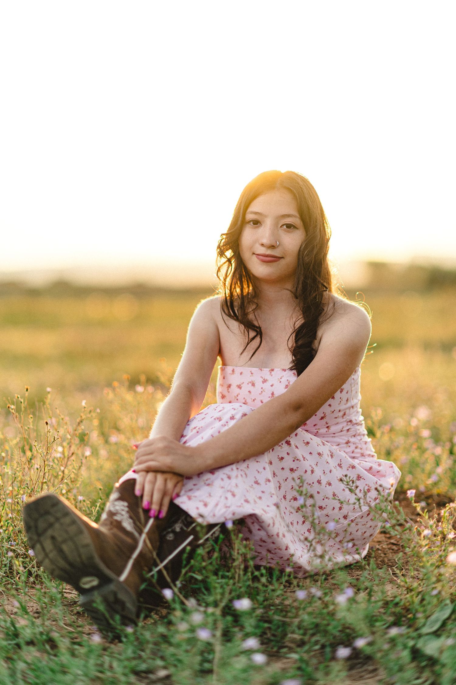 Person in a floral dress sitting in a wildflower meadow at golden hour.