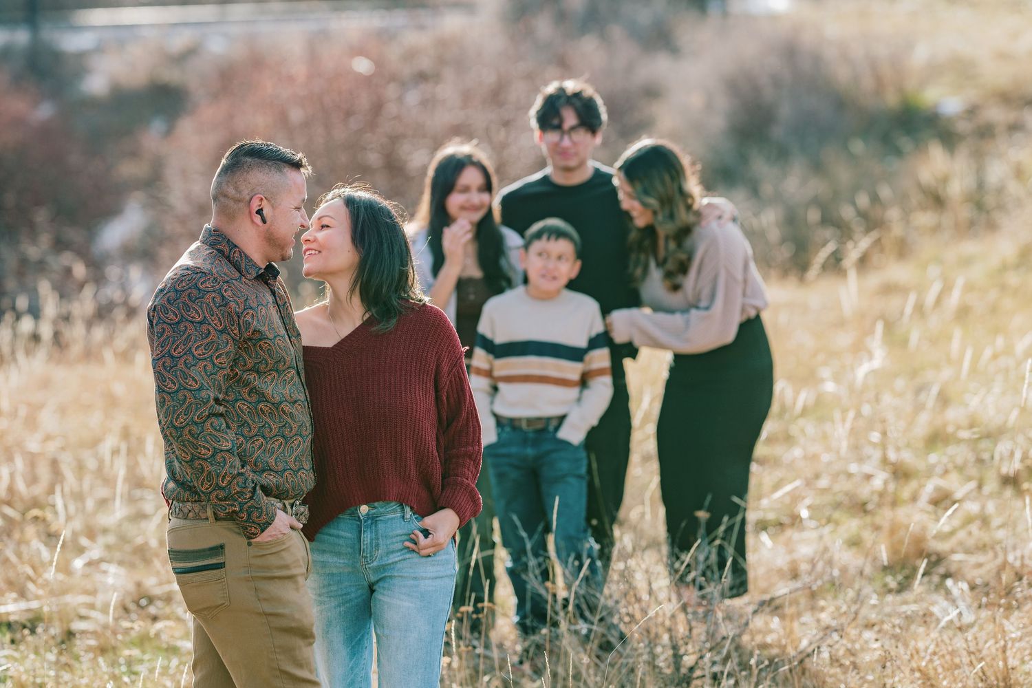 A group stands together in a golden field during sunset, creating a warm and intimate outdoor portrait.