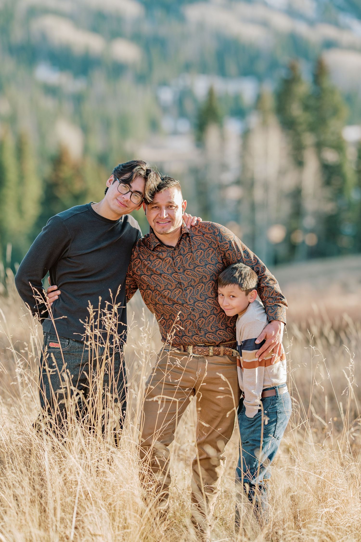 Two people sharing a tender moment while standing in a golden field of tall grass with mountains in the background.