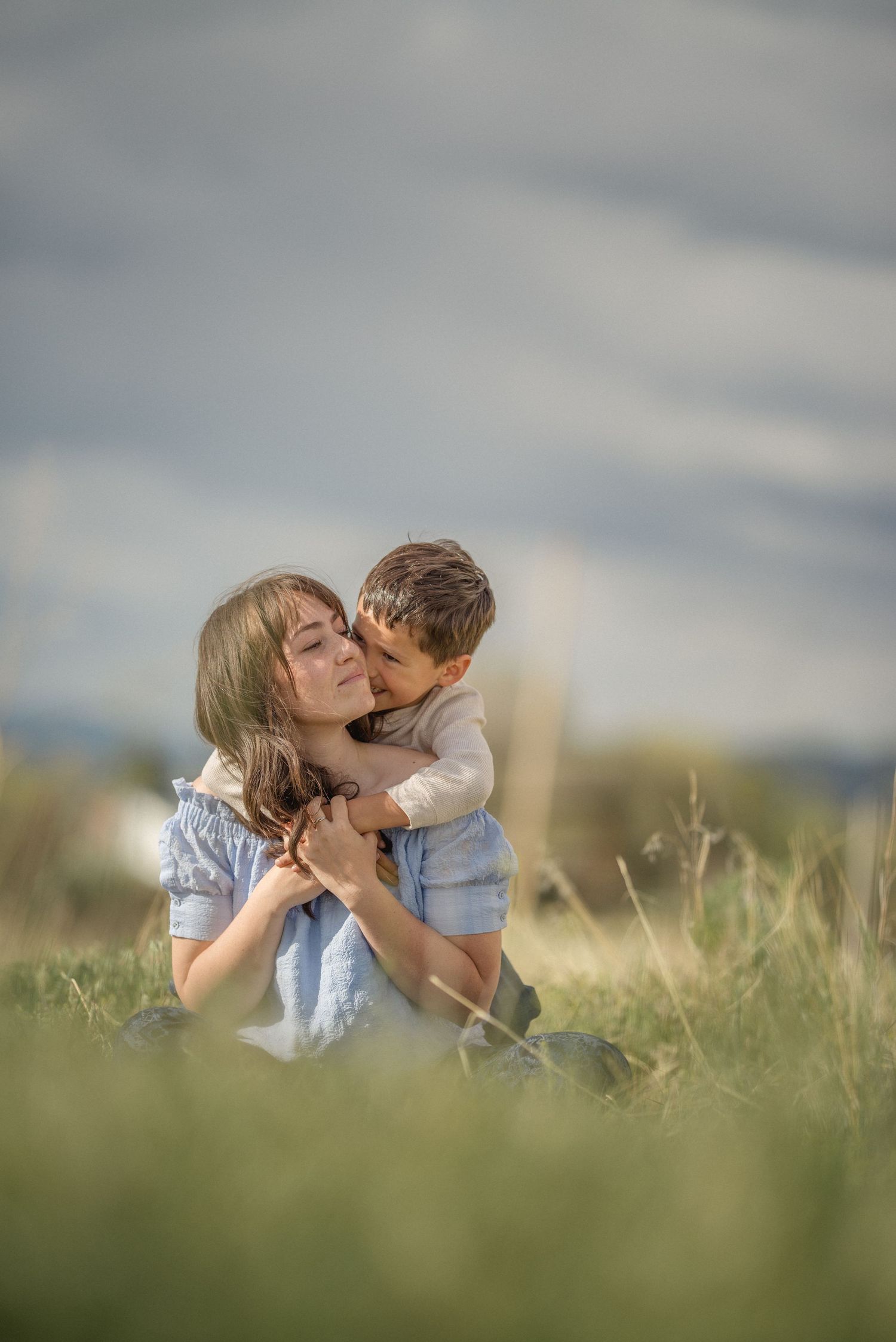 A tender moment shared between a parent and child embracing in a sunlit meadow on a cloudy afternoon.