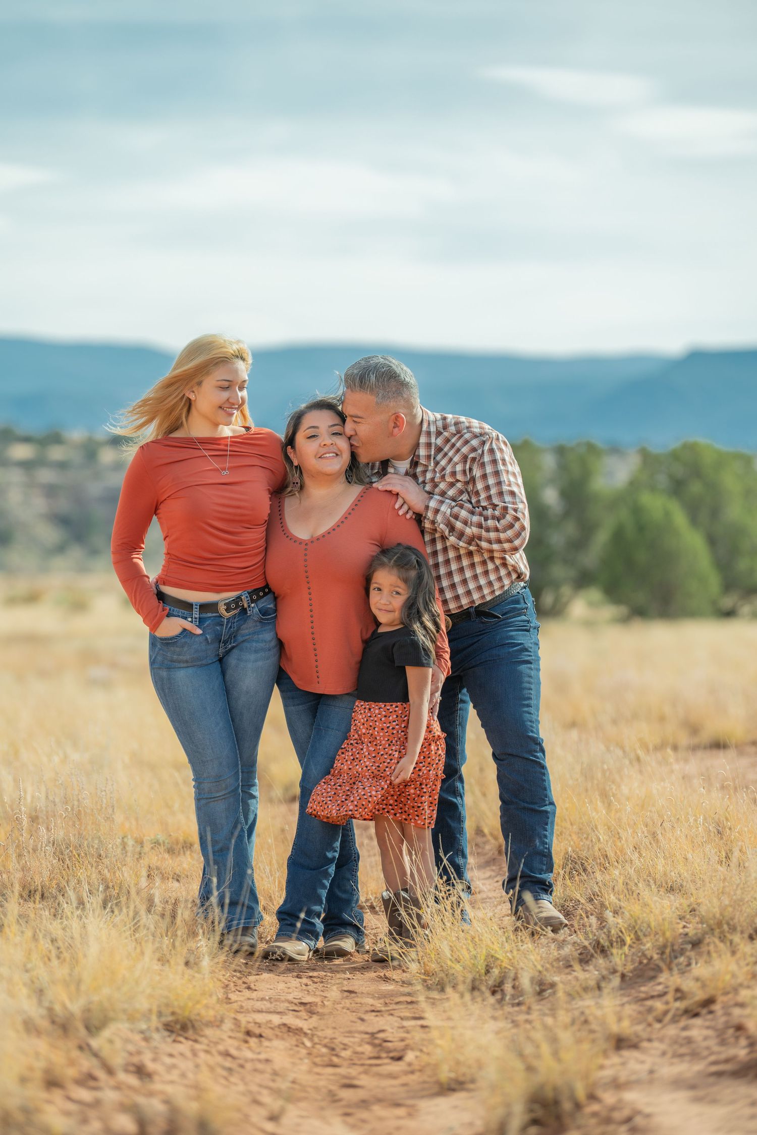 Family of three shares an intimate moment together while standing in a golden field during sunset.