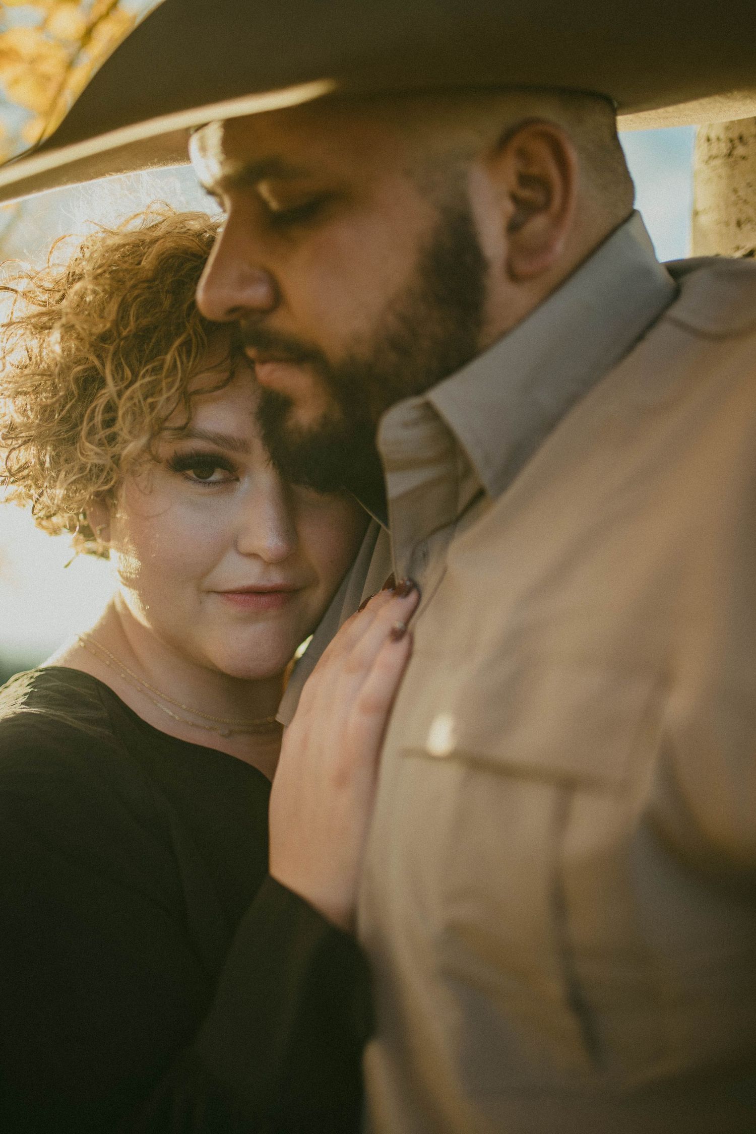 An intimate portrait of a couple embracing outdoors during golden hour, with soft sunlight illuminating their tender moment.