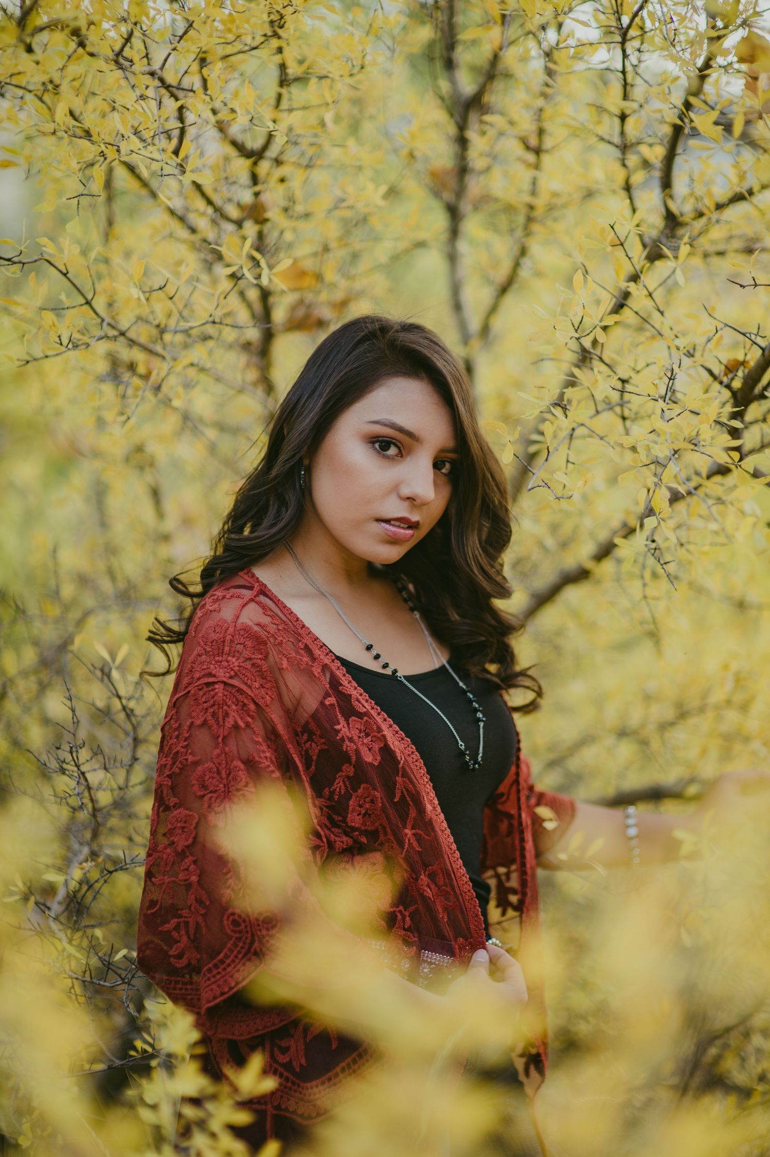 Portrait against yellow autumn foliage wearing a burgundy lace top and black dress.