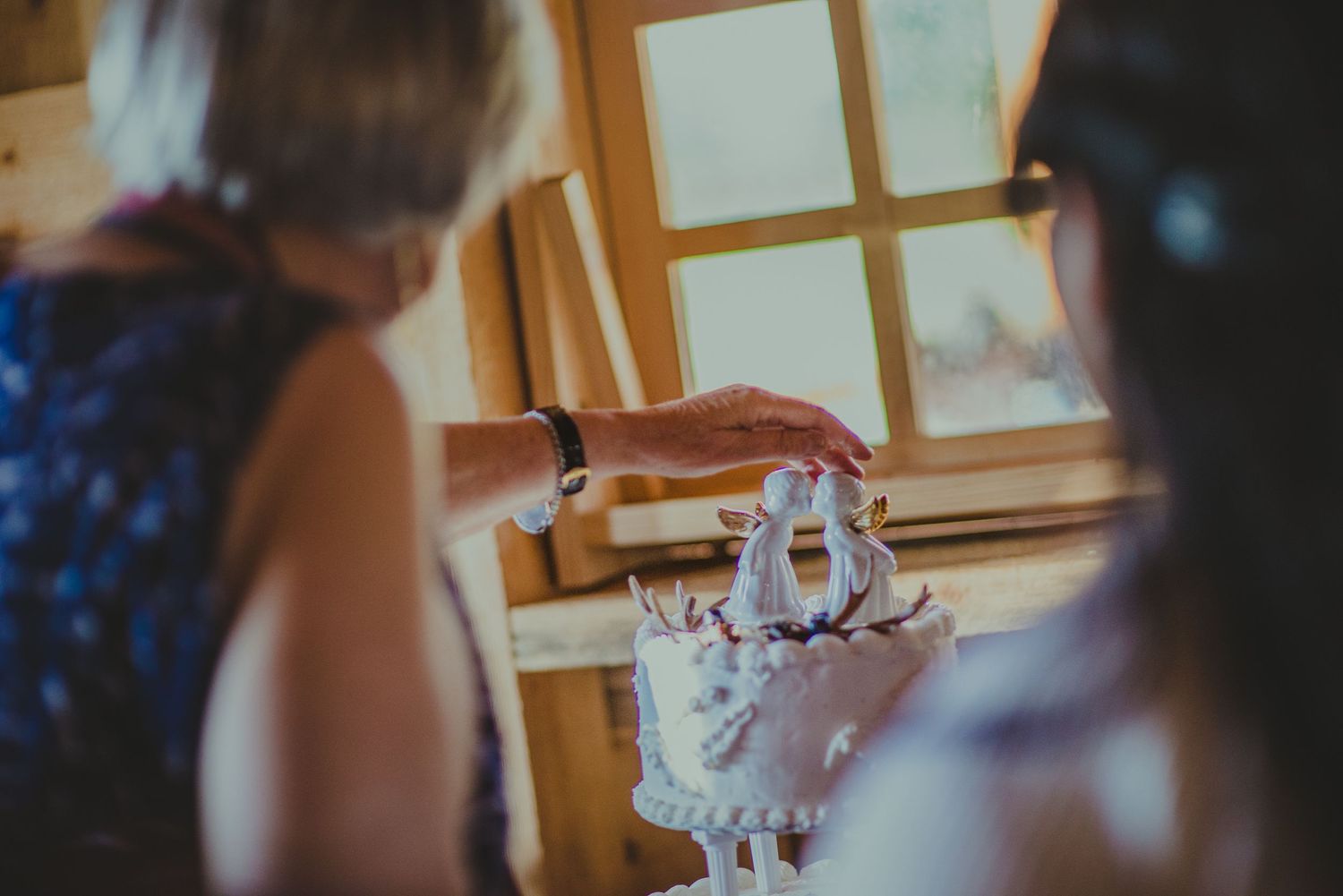 A three-tiered white wedding cake being served at a rustic reception venue.