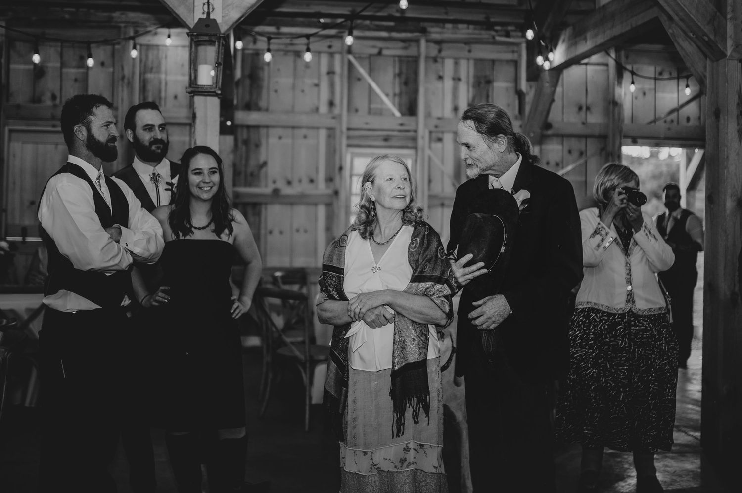 Black and white photo of wedding guests dancing and celebrating in a barn.