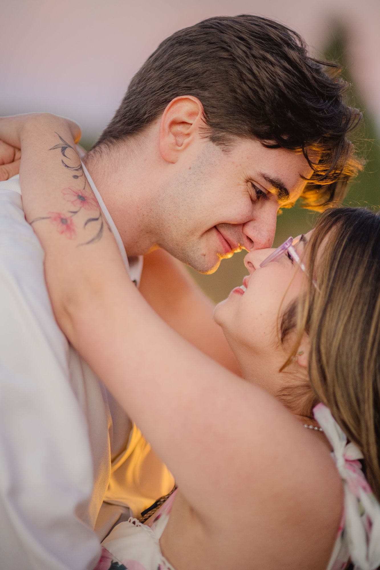 Couple leaning in for a kiss, floral tattoo on her arm, at their engagement session in Chama, NM.
