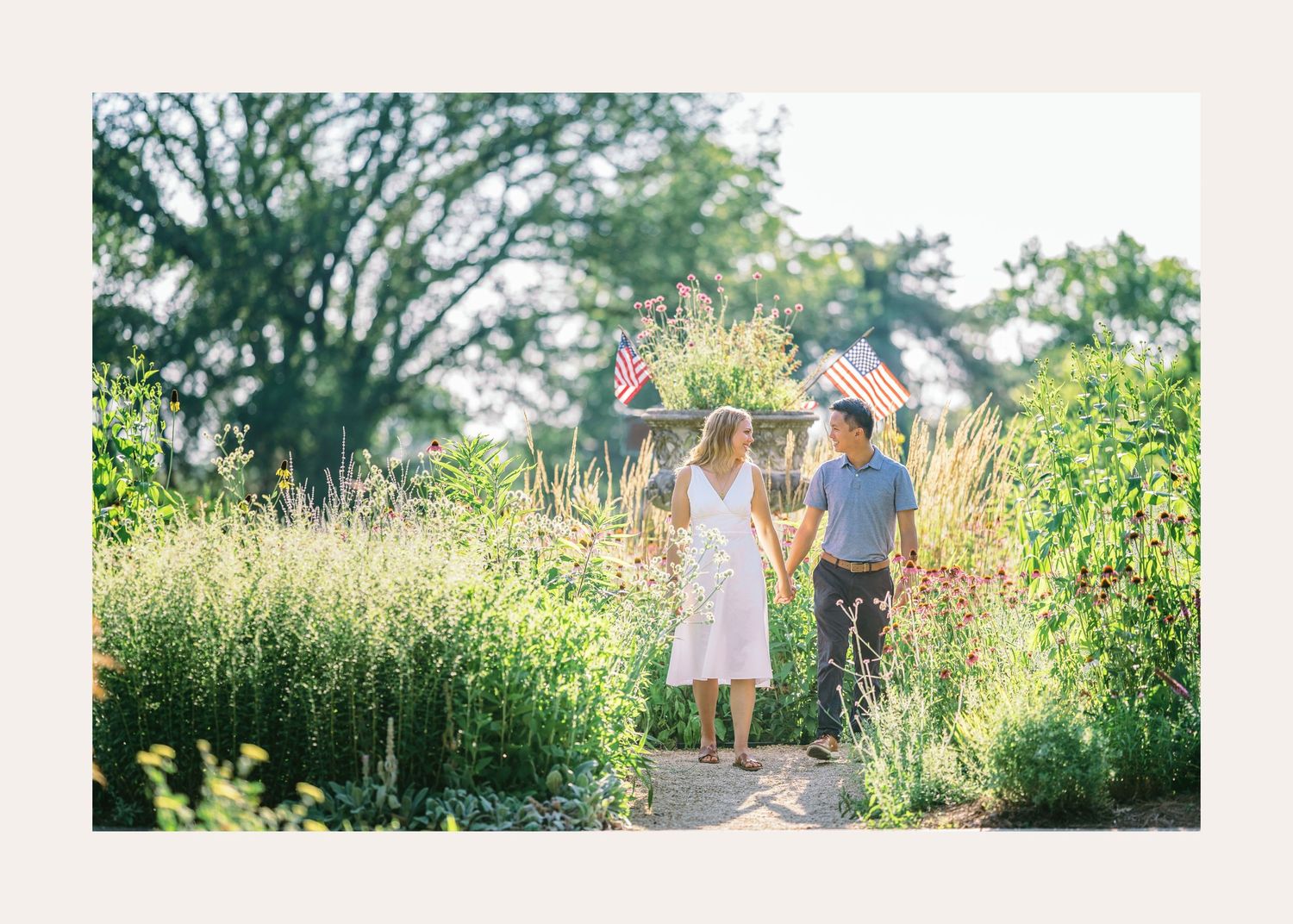A romantic summertime scene of a couple walking along a sunlit garden path surrounded by tall grass and greenery.