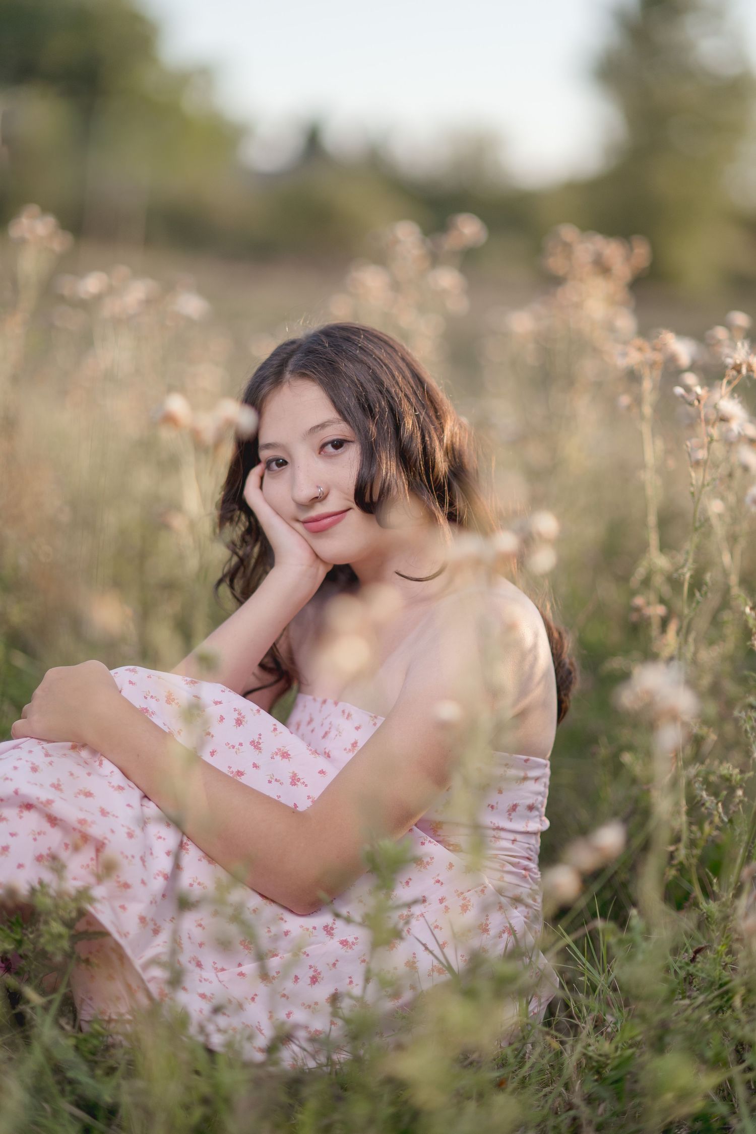 Dreamy portrait in a wildflower meadow showing someone in a pink floral dress laying among tall grass and flowers.