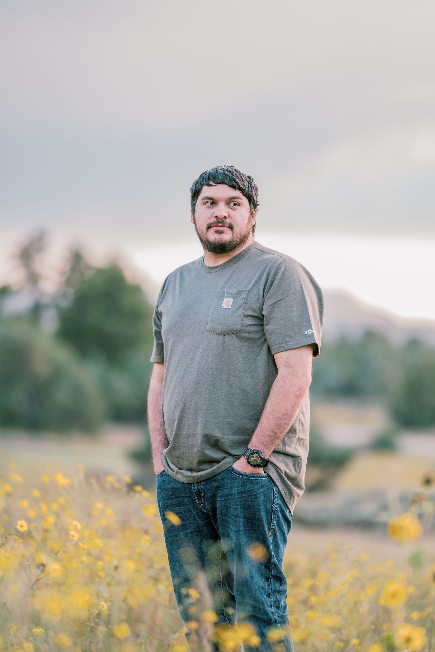 Person in grey t-shirt and jeans standing in a meadow of yellow flowers at sunset.