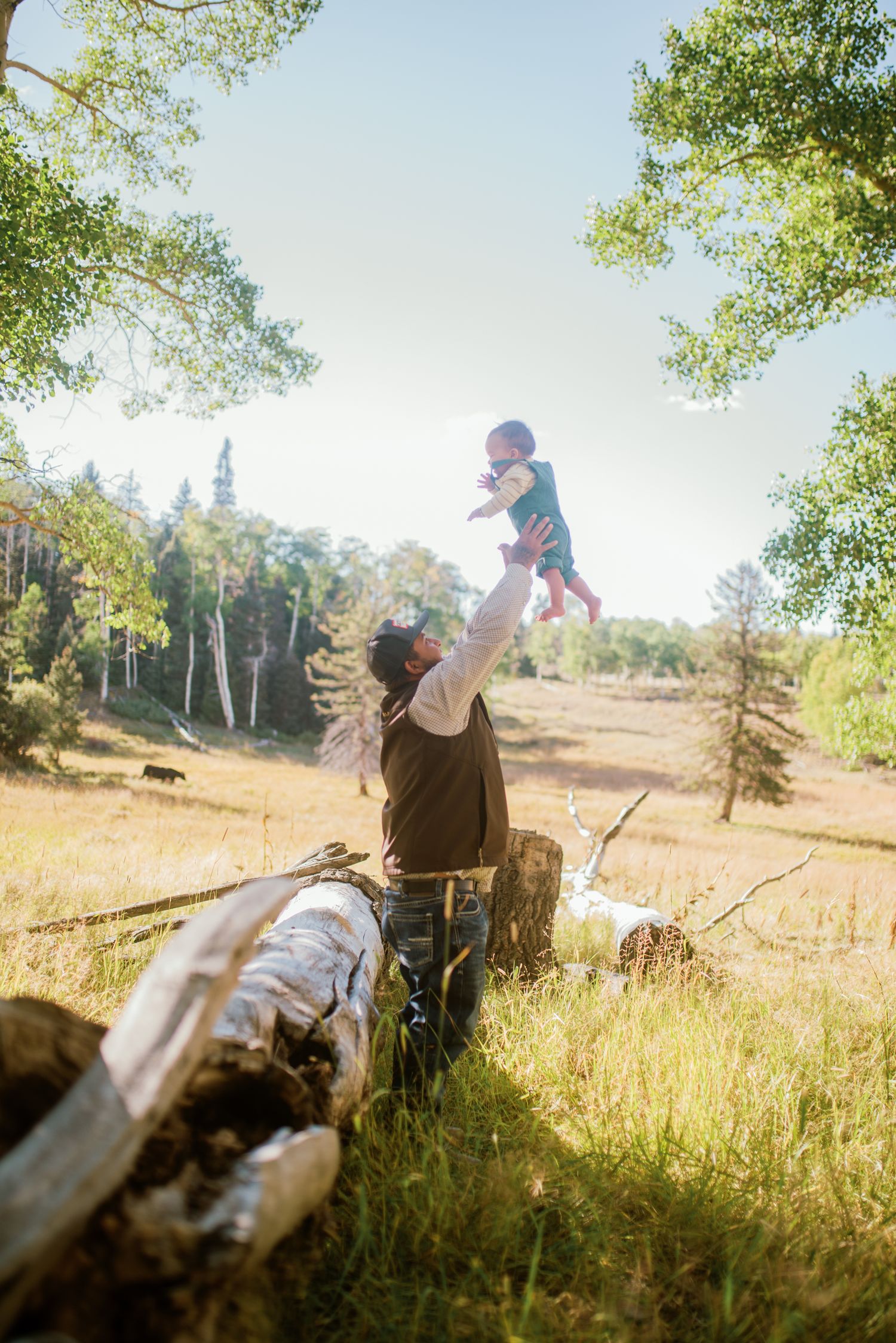 Father holding his 1-year-old son amidst tall forest trees — candid, heartfelt moment by Quiet Light by The Amora