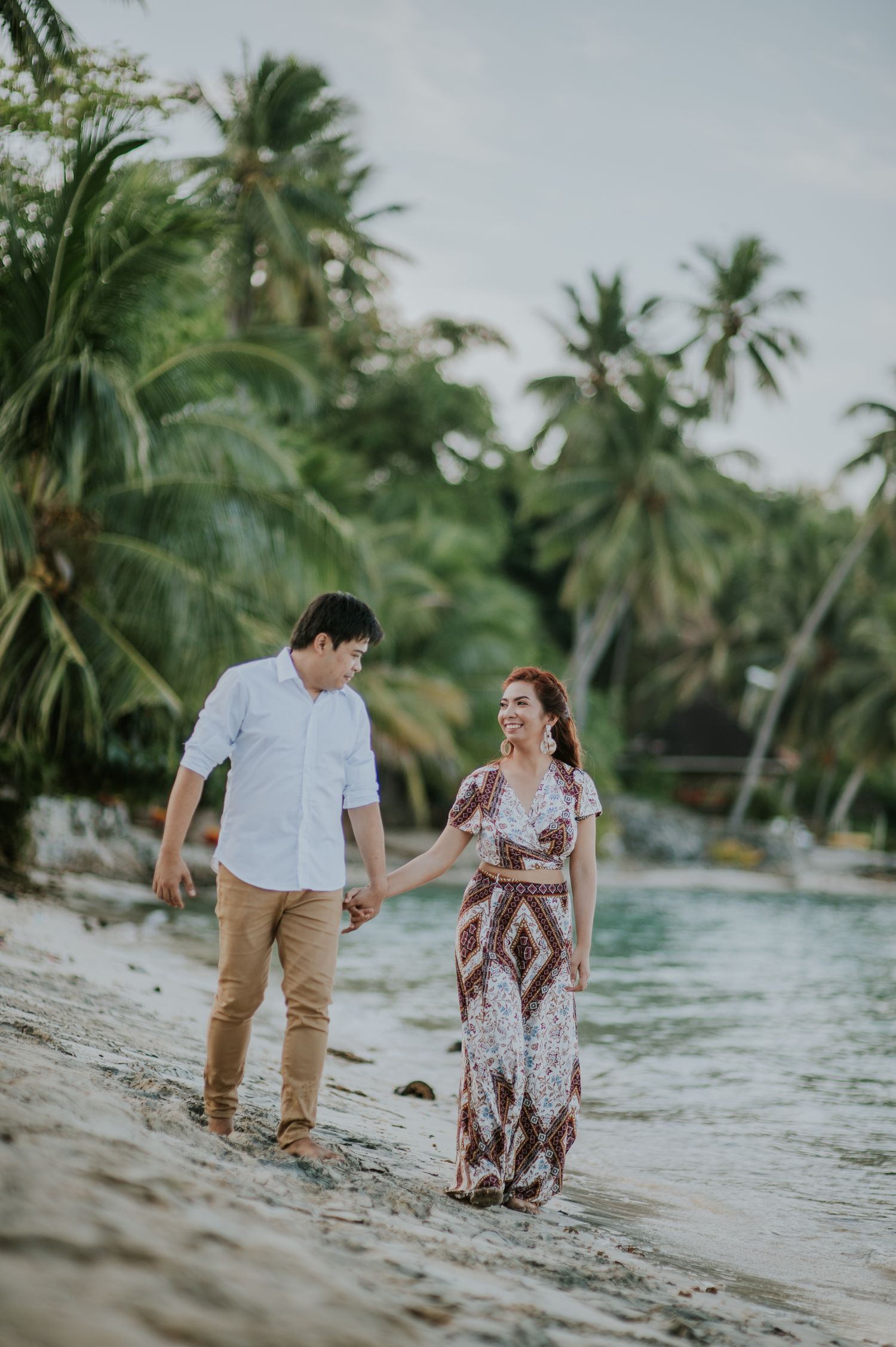 A romantic beach photoshoot with palm trees and gentle waves in the background.