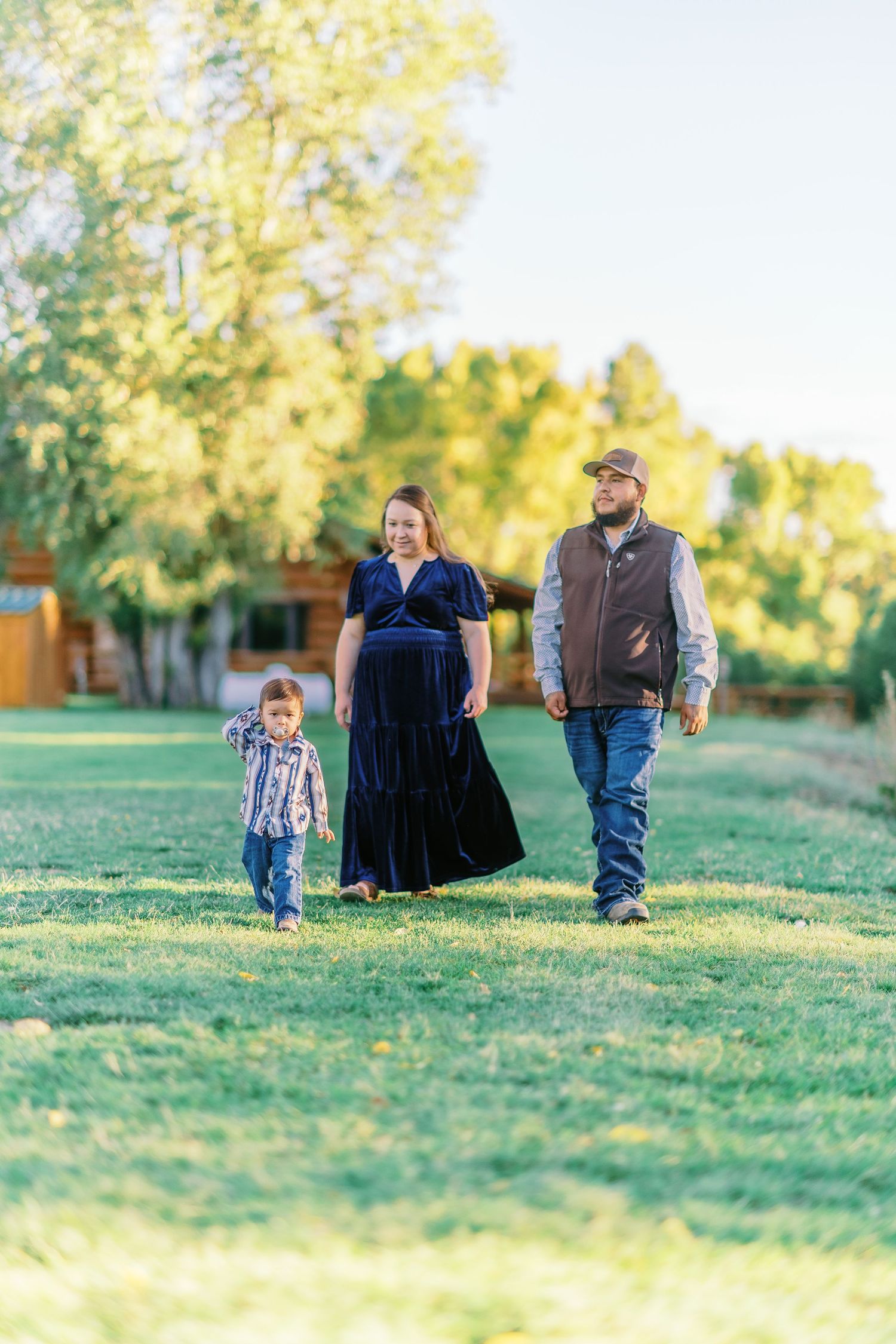 Family sits together on grassy hill during golden hour autumn photo session in park.