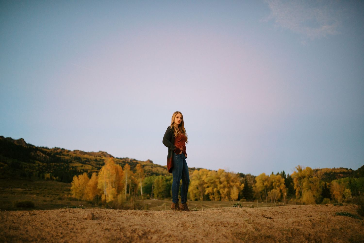 Silhouettes of people standing against a scenic sunset landscape with rolling hills create a dramatic panoramic view.