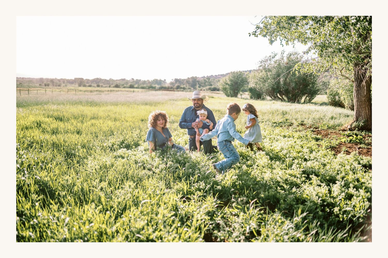 Family sitting together in a lush green field on a sunny day, with trees and open farmland in the background.