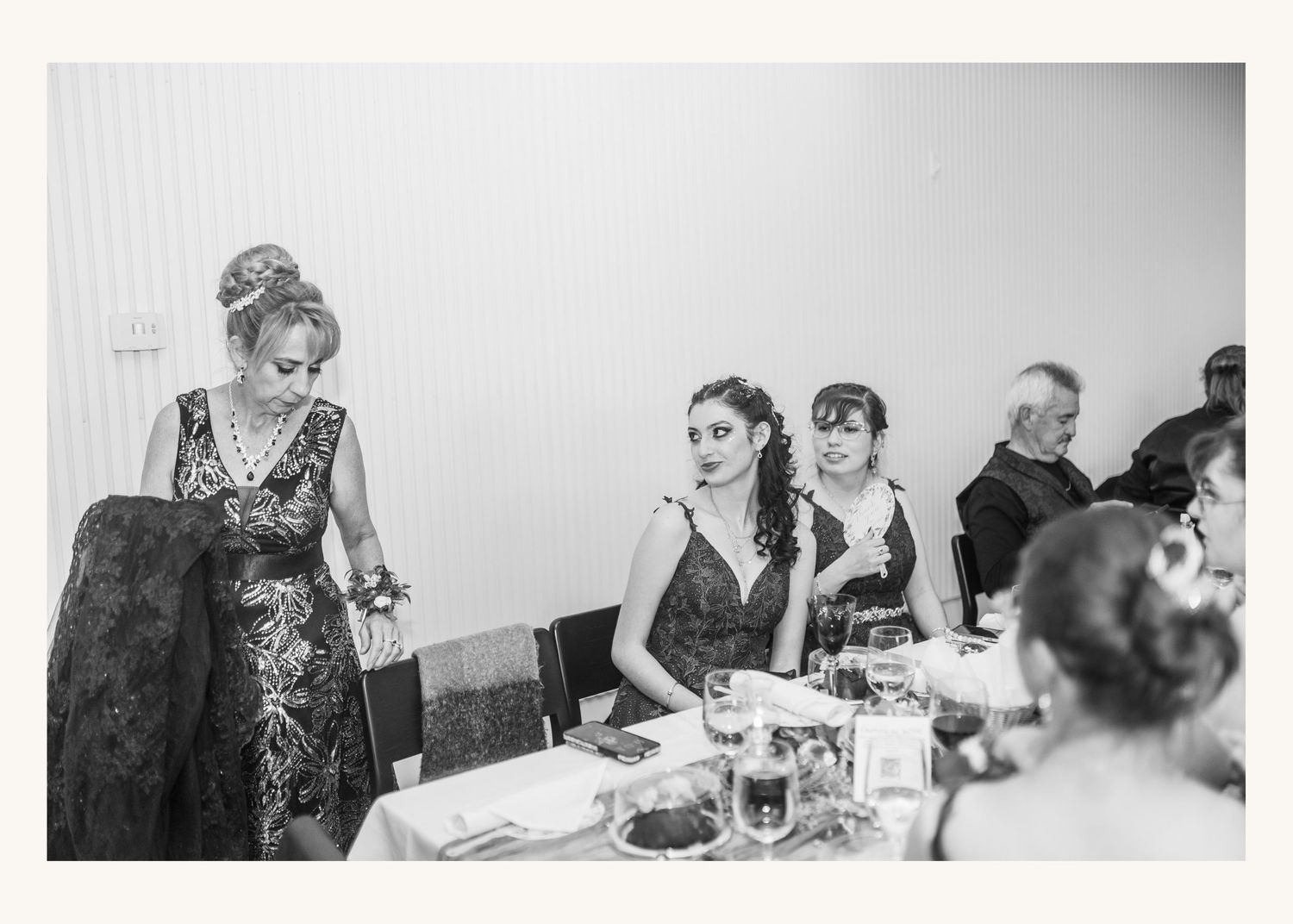 Black and white wedding reception photo of elegantly dressed women at a formal dinner table.