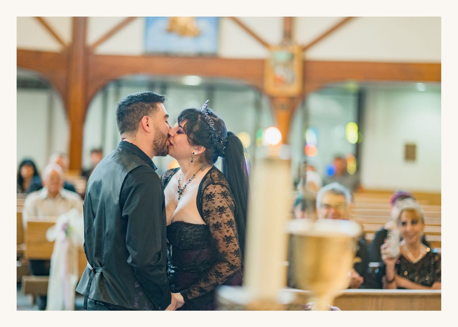 Couple sharing first kiss at church wedding altar with guests seated in pews during ceremony.