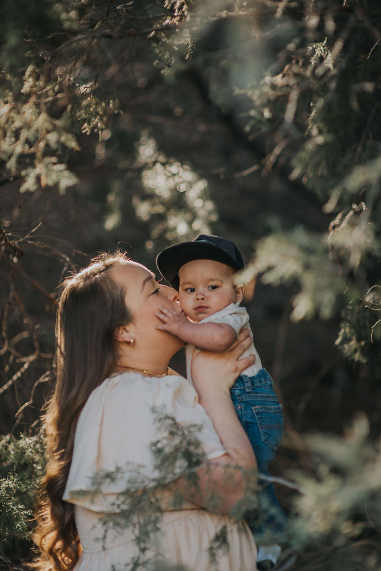 Mom holding her toddler beneath towering pines in northern New Mexico — natural light portrait by The Amoras.