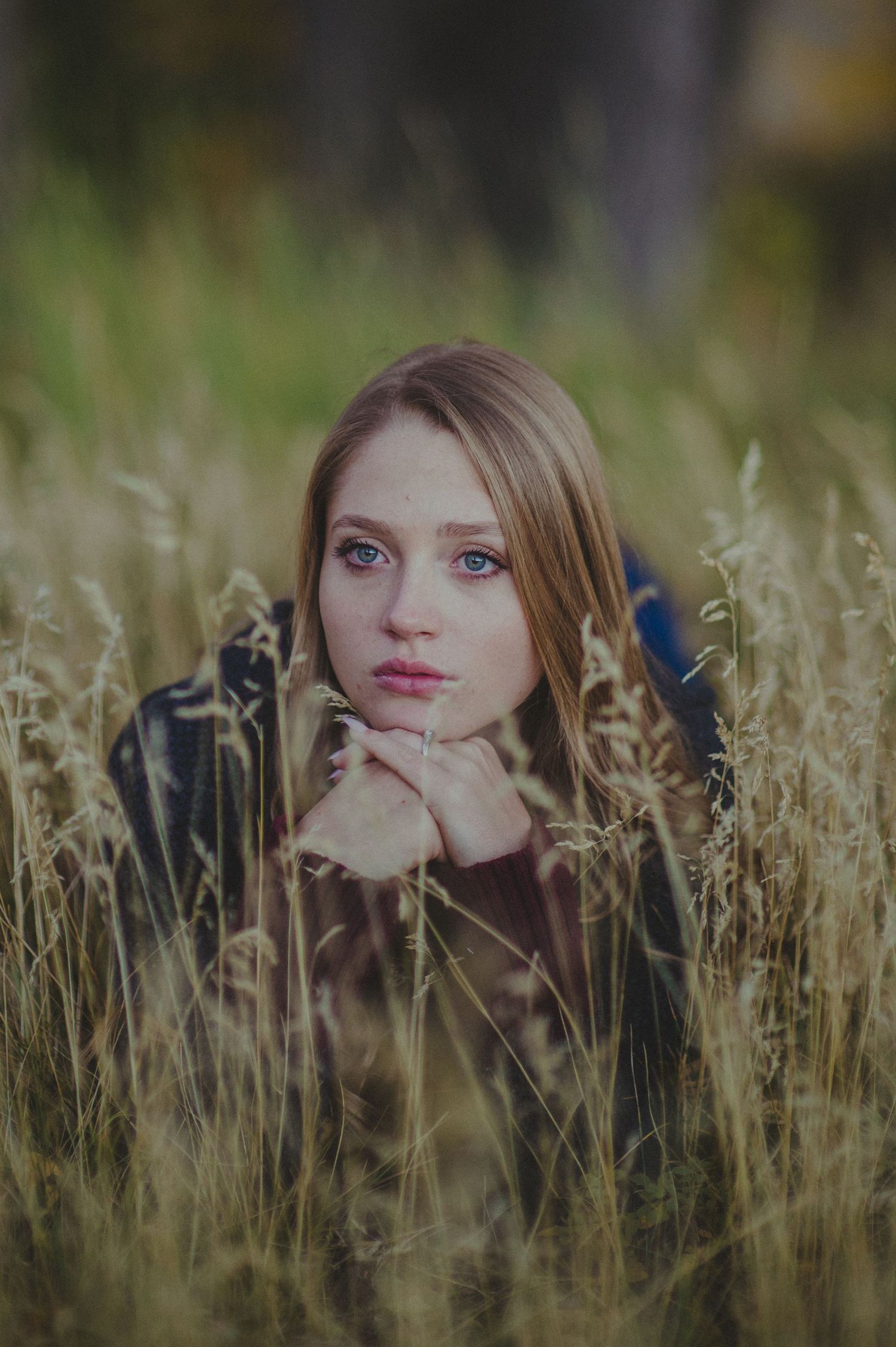 A woman with striking blue eyes peeks through golden wheat stalks in this dreamy outdoor portrait series.