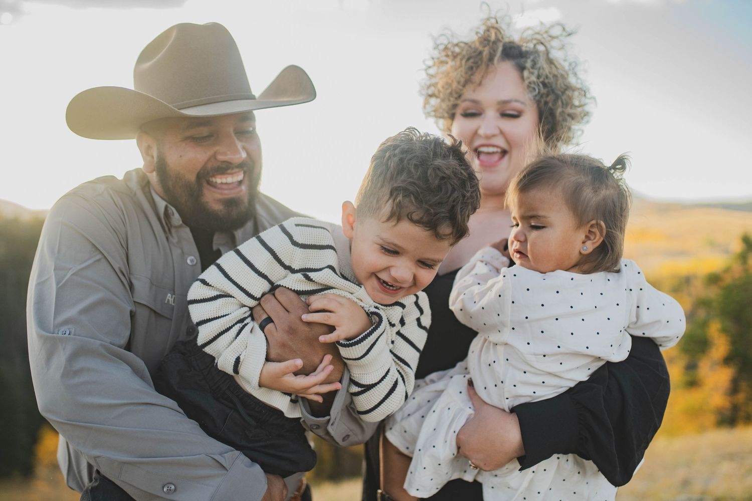 Mom and dad playing with their toddlers in a golden autumn field — joyful family moment by Quiet Light by The Amoras in New Mexico.