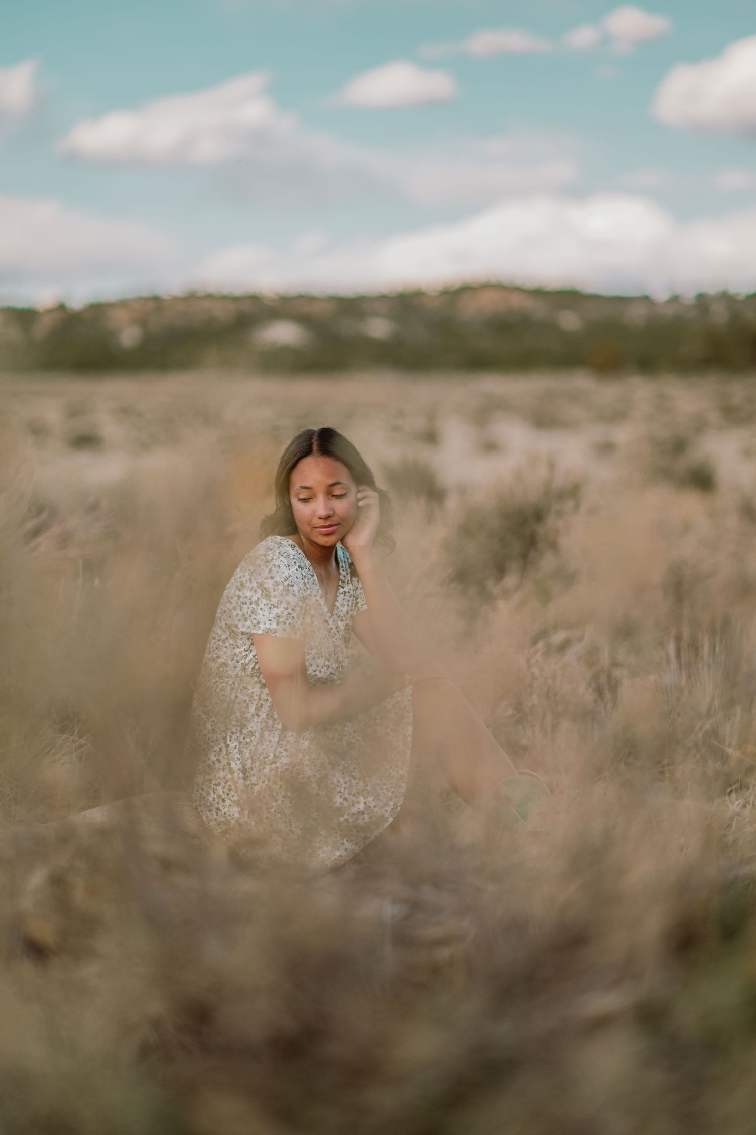 Woman in sparkly dress poses thoughtfully in desert landscape with golden light and desert brush surroundings.
