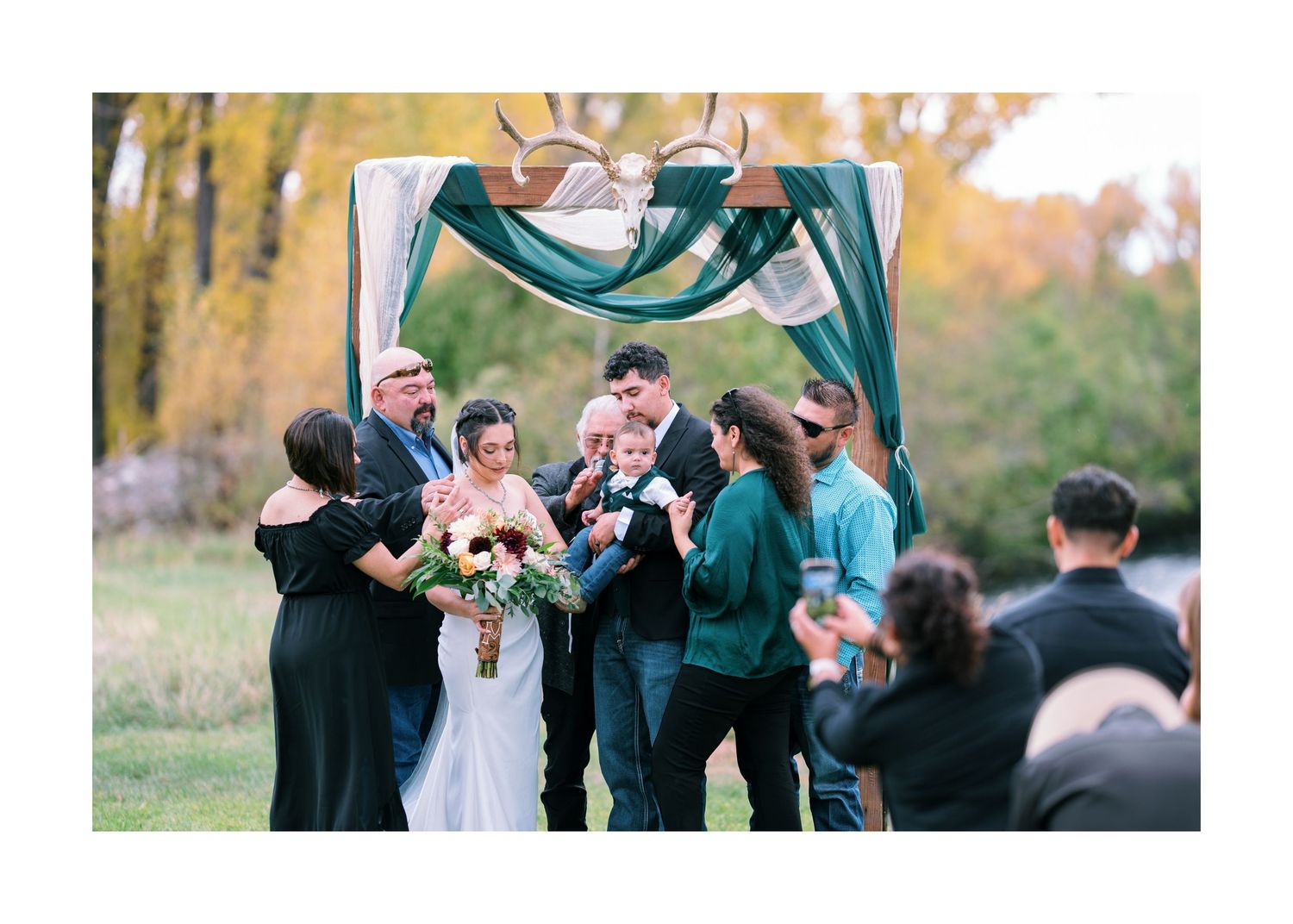 A joyful outdoor wedding ceremony with guests gathered under autumn trees.