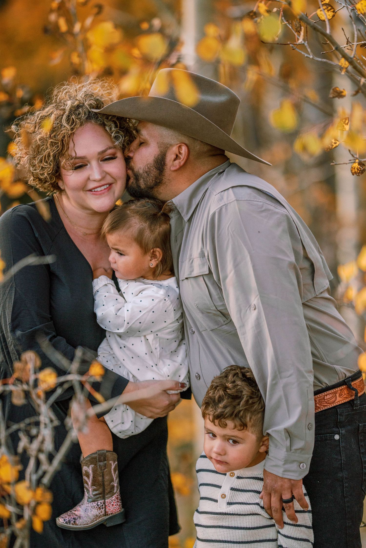 Family embraces in a tender moment amid golden autumn foliage wearing western attire.