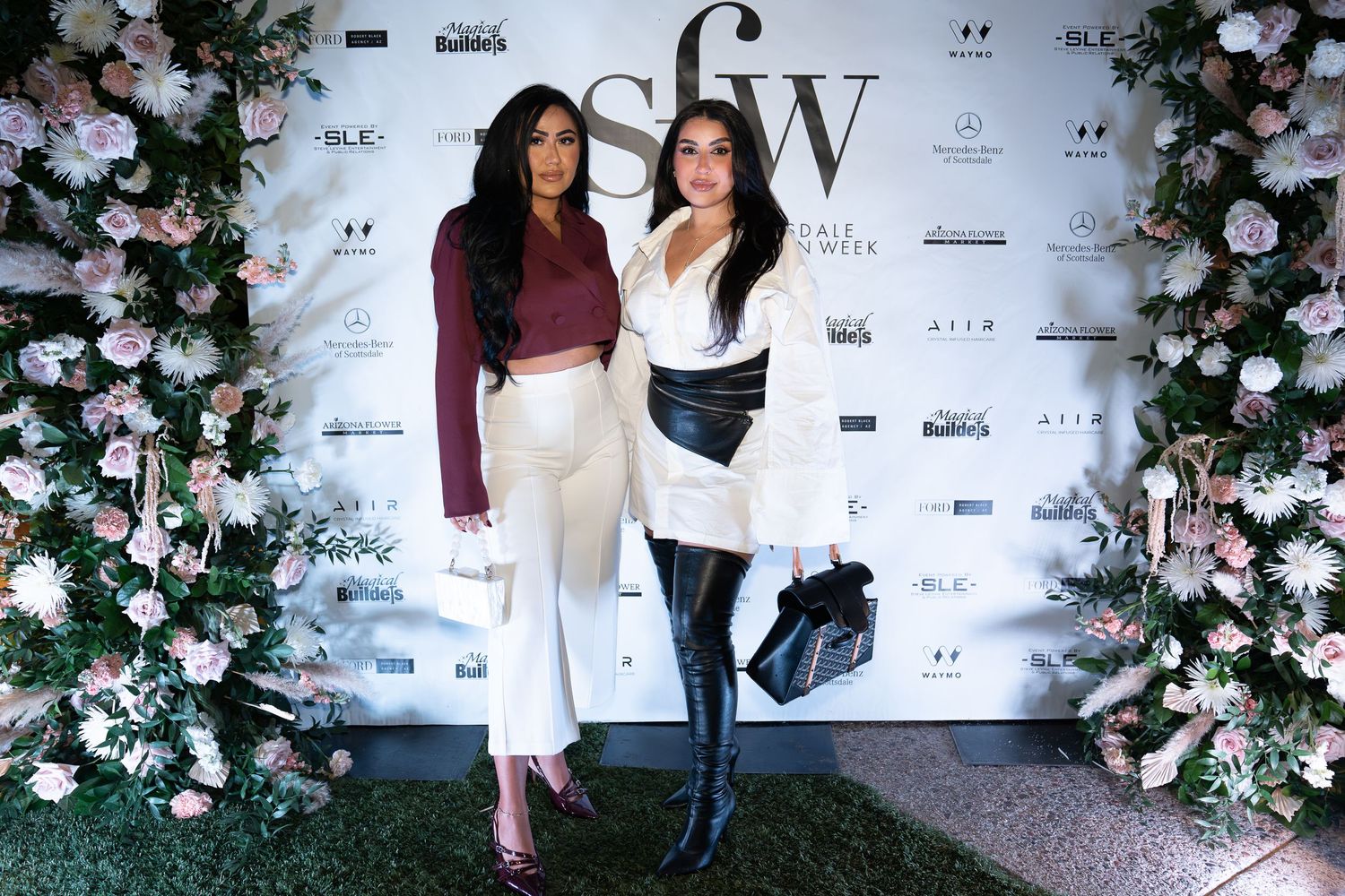 woman wearing a maroon, long sleeved crop top blouse with white pants, woman wearing a long white long sleeved blouse with a black belt