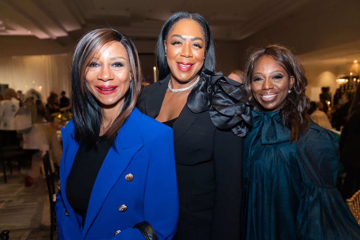 woman with a blue blazer, woman with a black blazer that has a faux flower on shoulder, woman wearing a teal dress