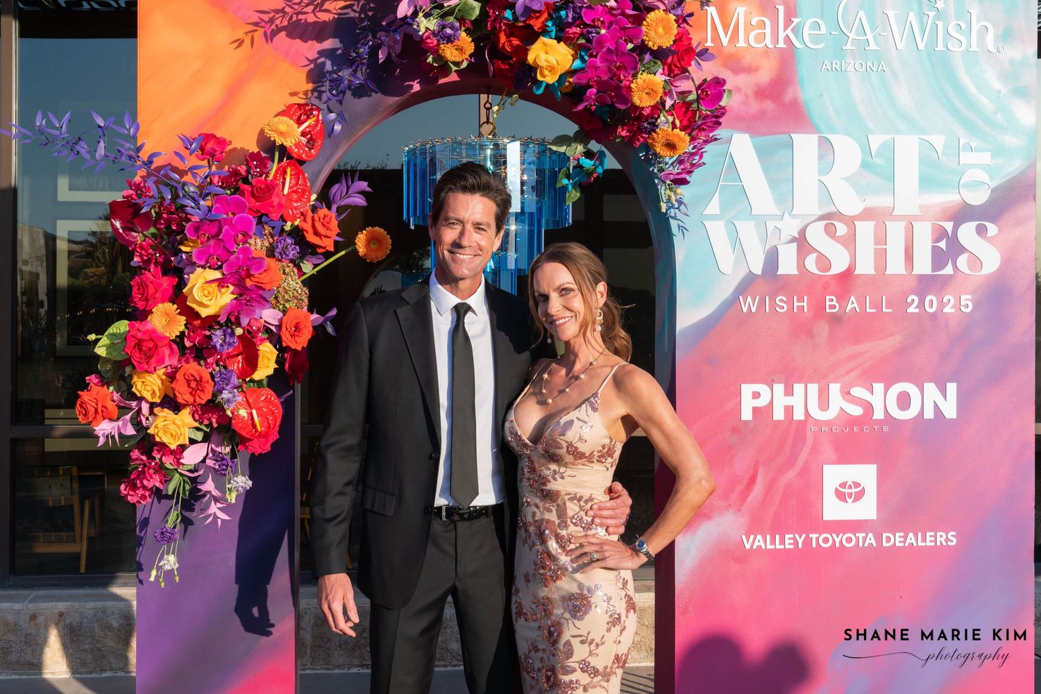 man wearing a black suit and grey tie, woman wearing a gold floral dress
