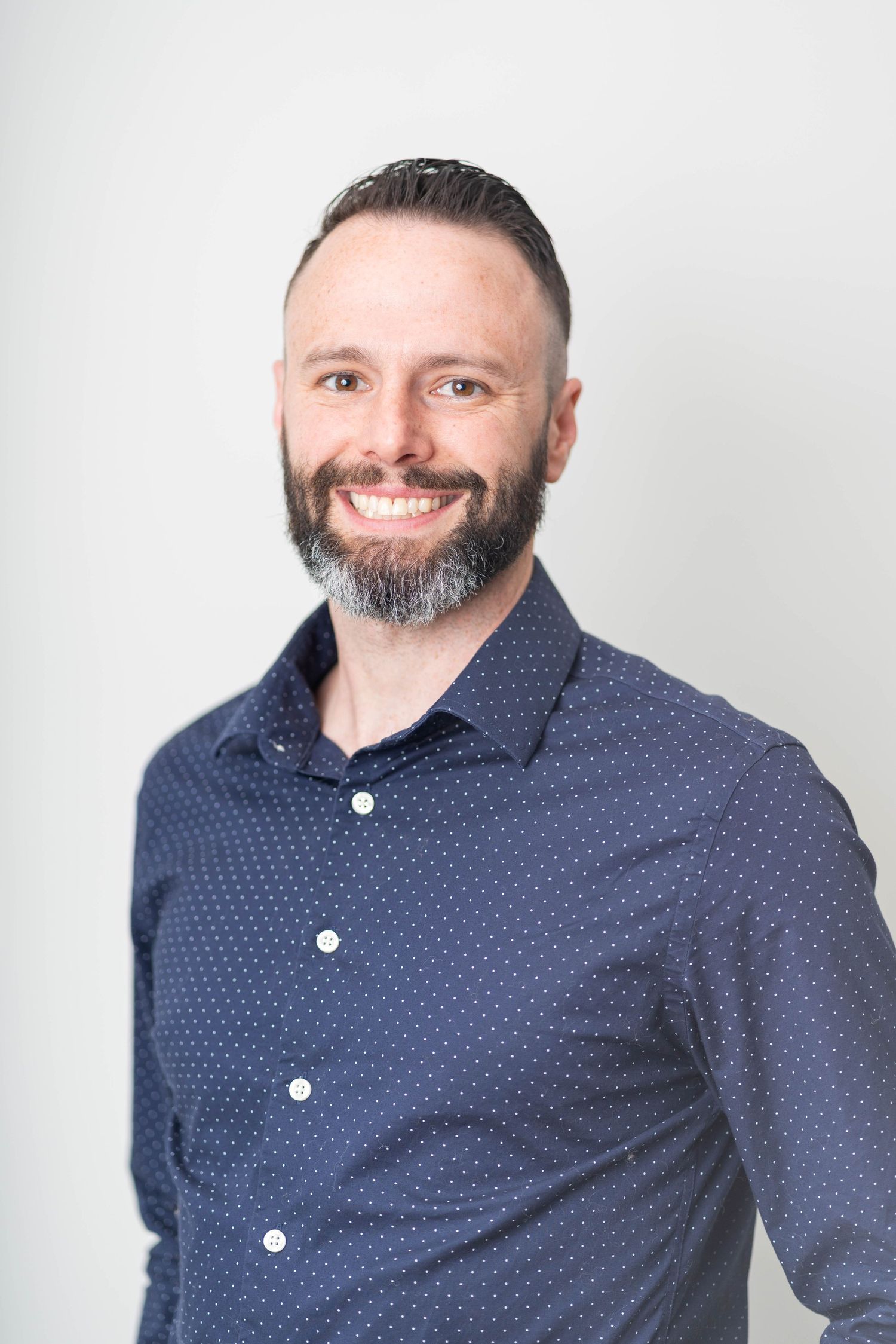 man with a beard, wearing a blue, polka dot long sleeved button up.