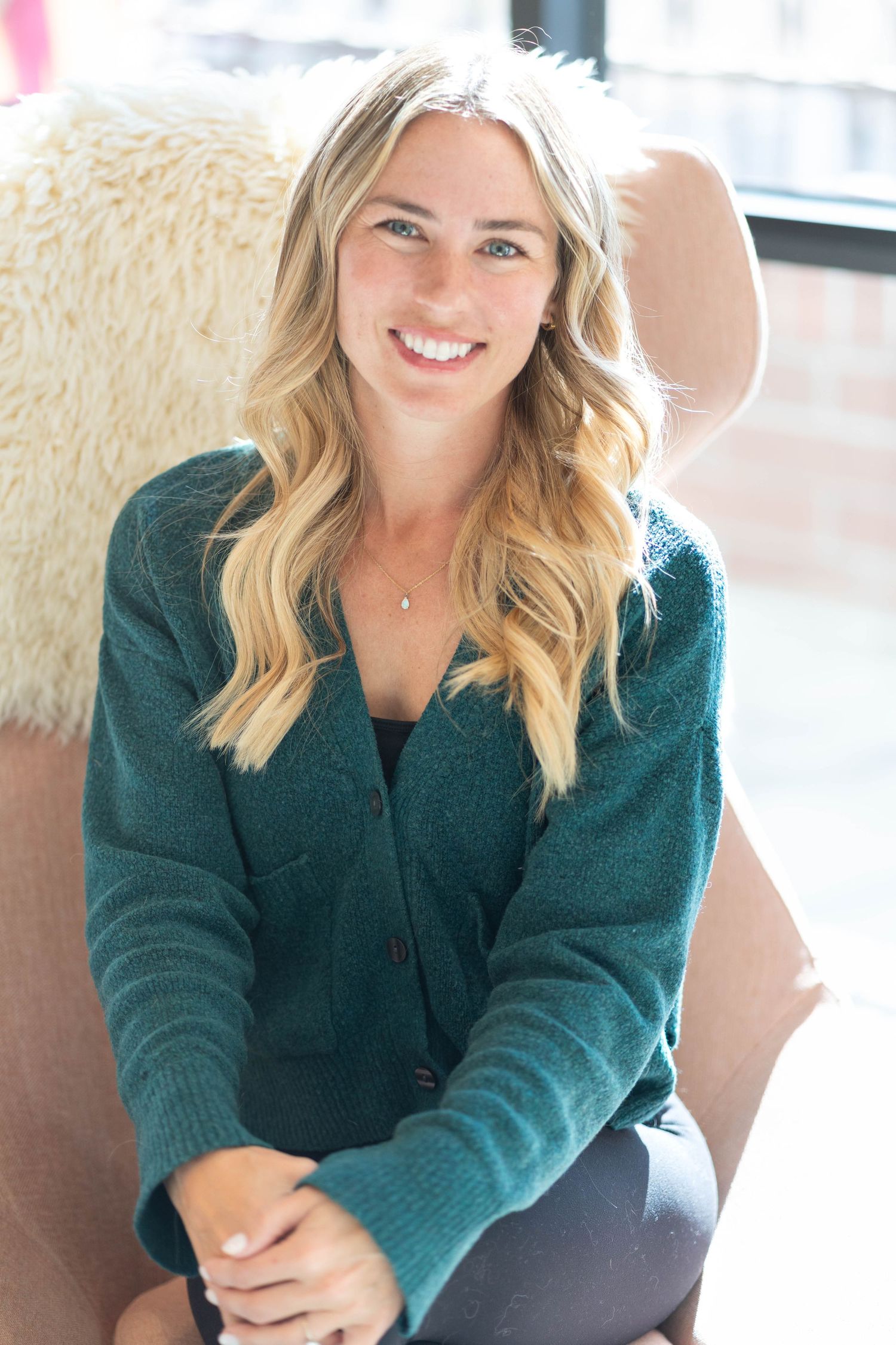 girl with blonde hair, wearing a forest green long sleeve, girl sitting on a pink chair