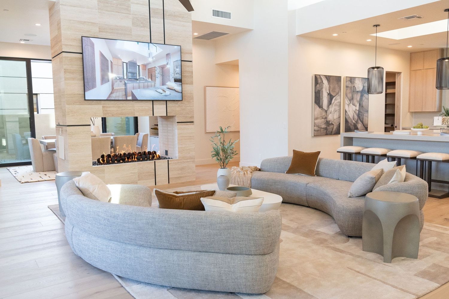 view of a living room area with grey couches, tv, fire place and the kitchen in the next room