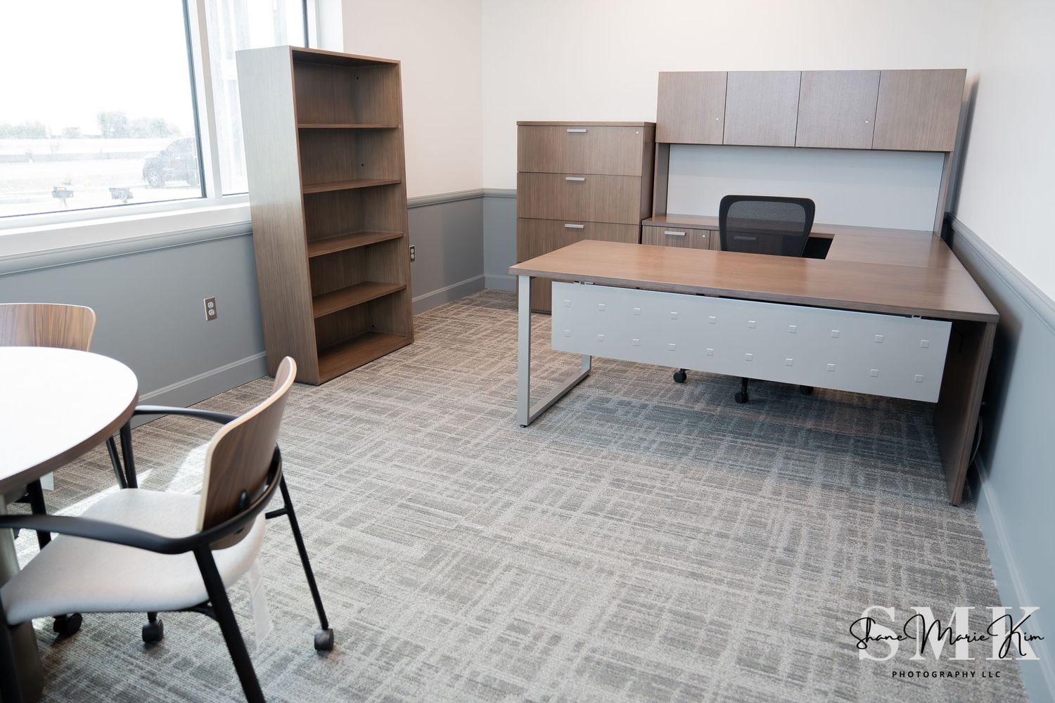 large office room with a window, L desk with a book shelf and extra drawers, circular desk with 4 chairs