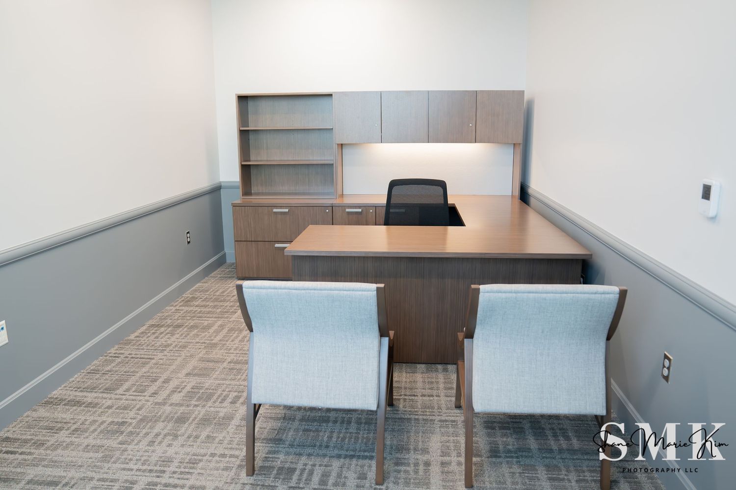 office room with an L desk, includes shelves, black desk chair and two office chairs for employees or guests