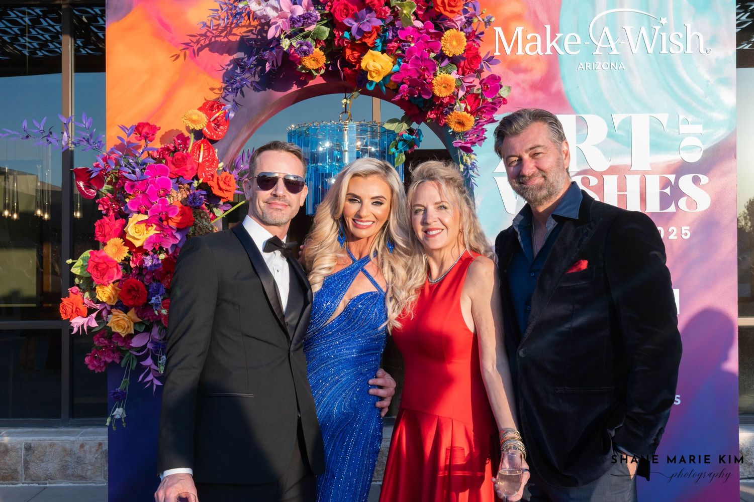 man wearing sunglasses and a black suit, woman wearing a blue dress, woman wearing a red dress, man wearing a black suit