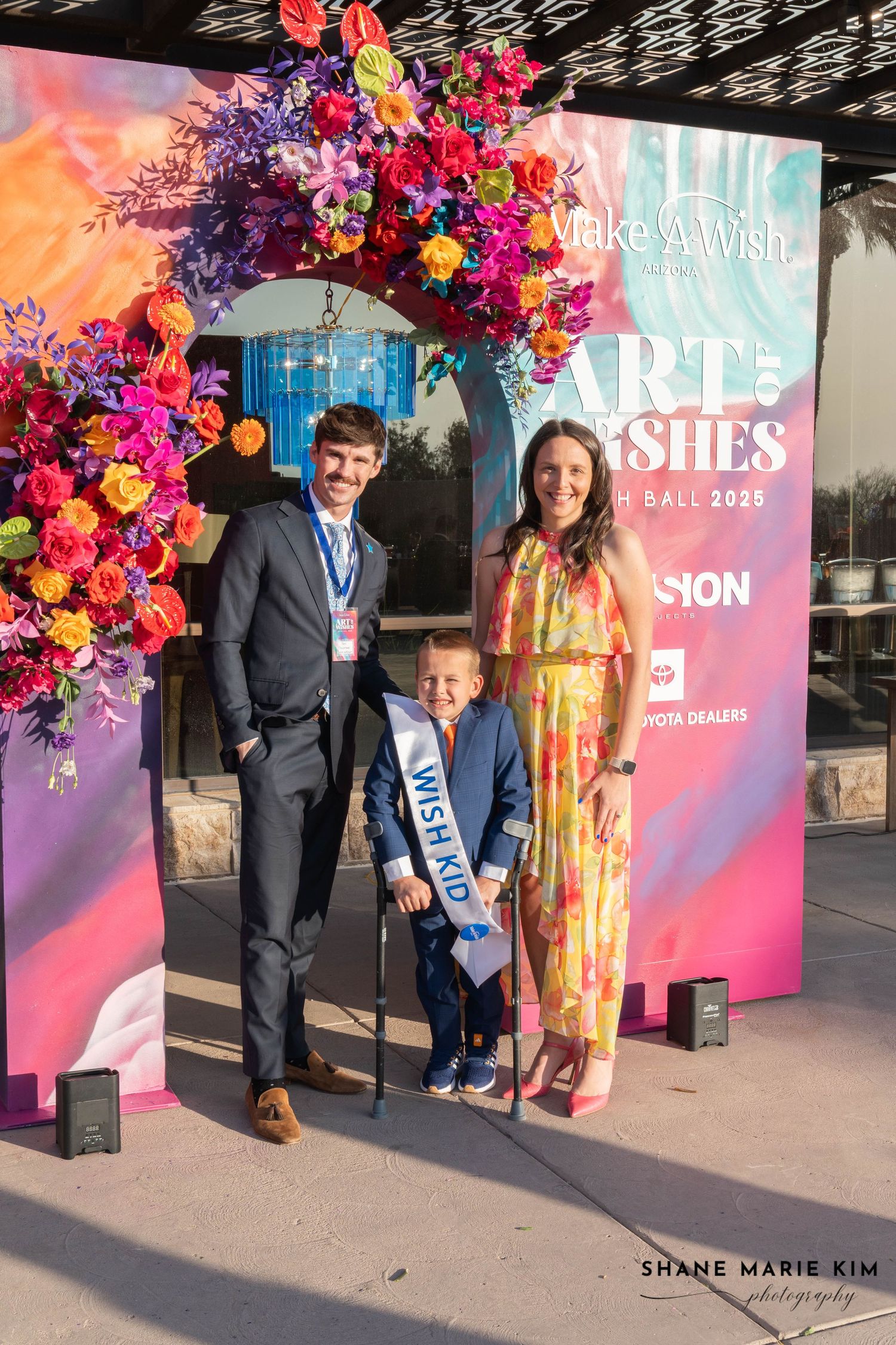 man wearing a pant suit, child wearing a pant suit, woman wearing a yellow floral dress