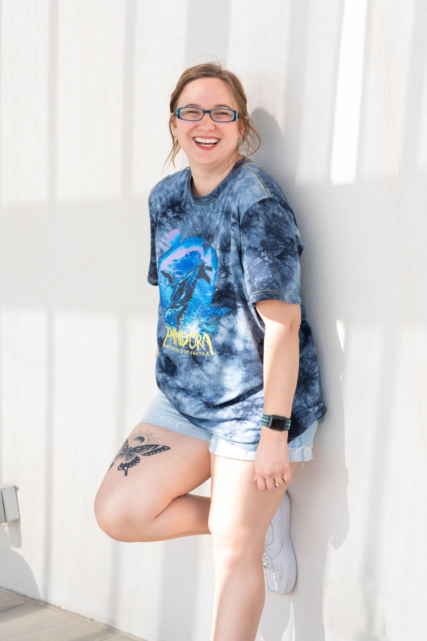 girl with a butterfly tattoo on thigh, girl wearing glasses, girl standing against the wall