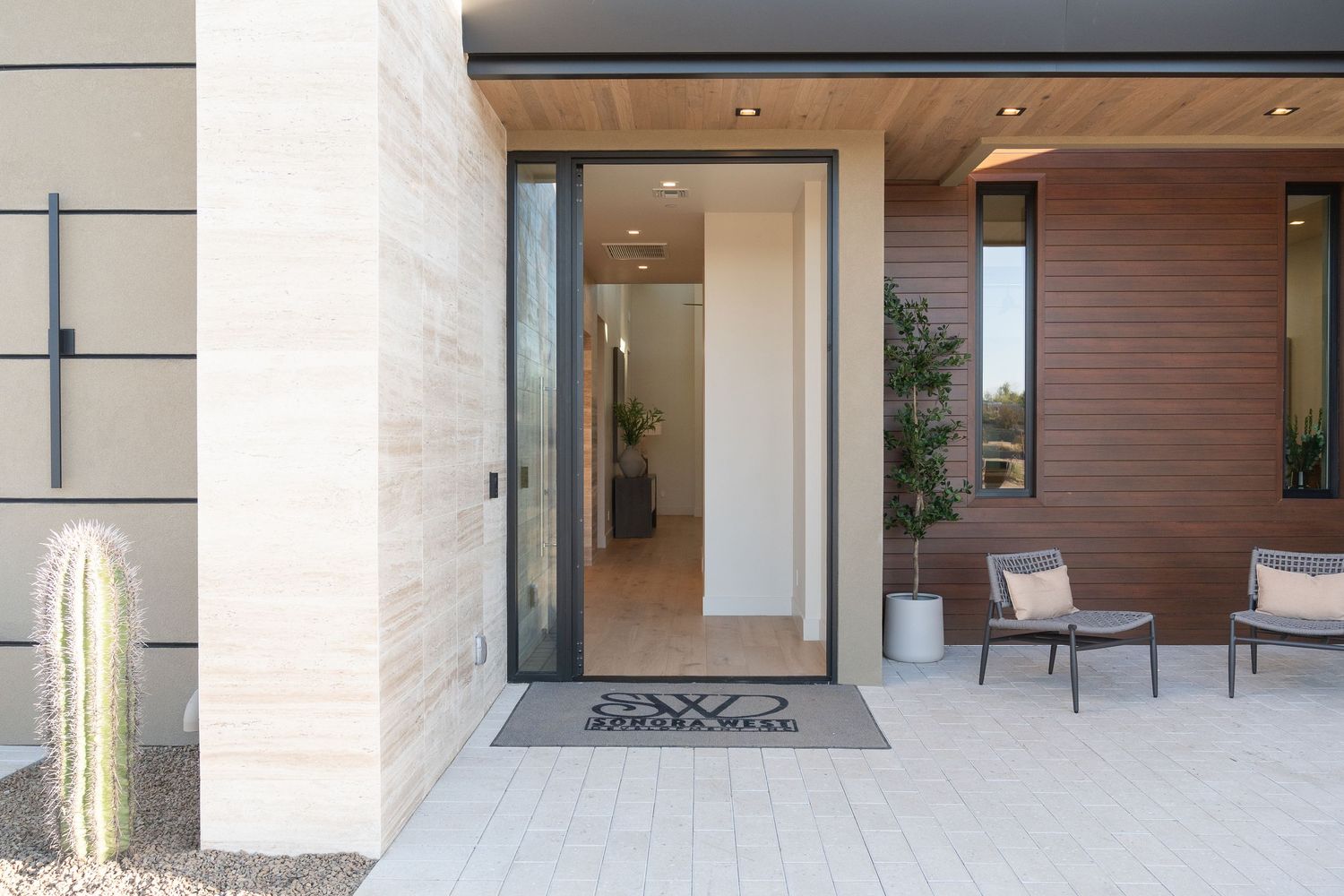 view of the front of a modern home, big wide doors, brownish reddish wooden walls with two chairs out front