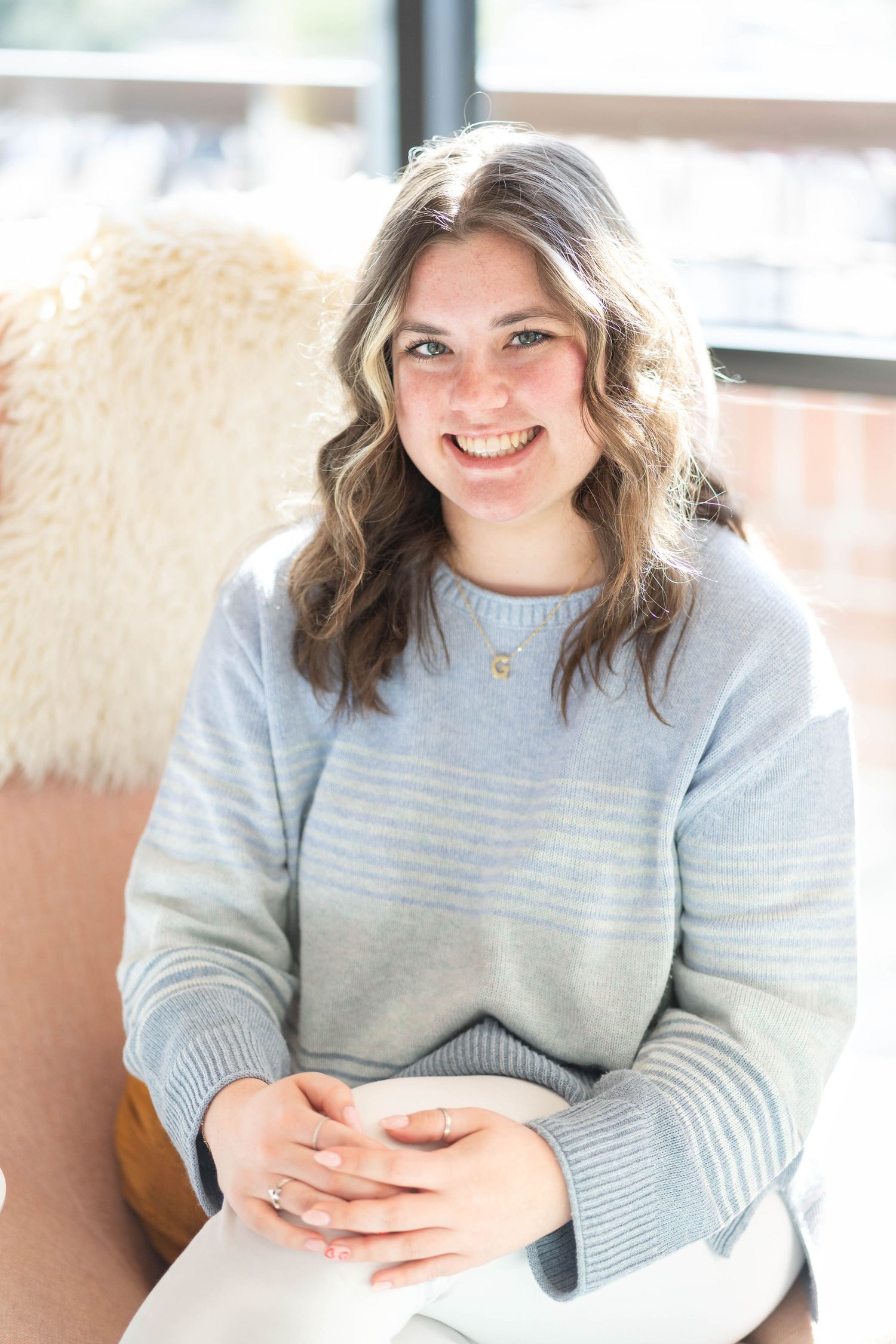 girl with medium length hair, girl sitting on a pink chair, girl wearing a stripped, blue and grey long sleeved shirt.