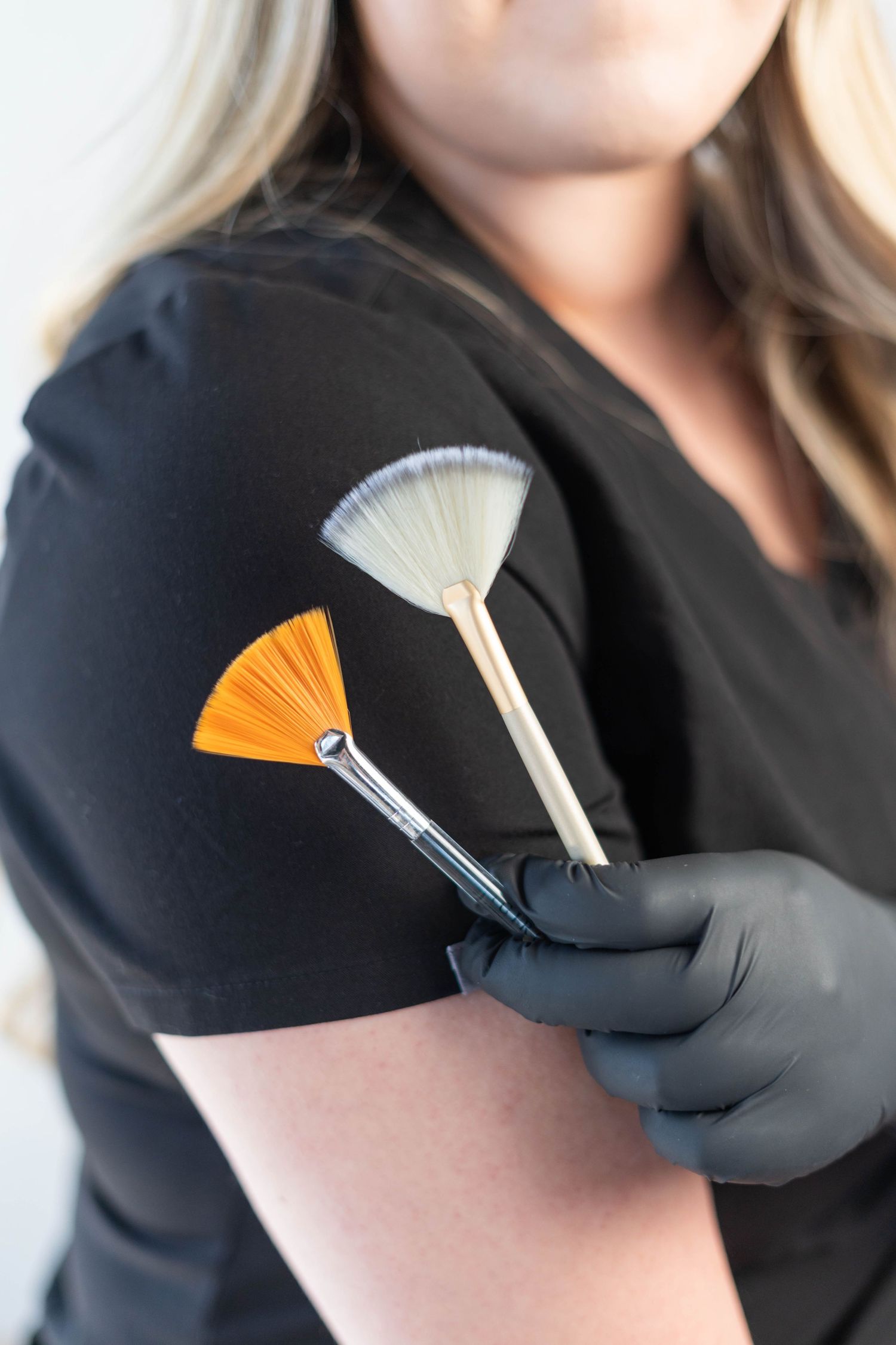 aesthetician holding two facial brushes