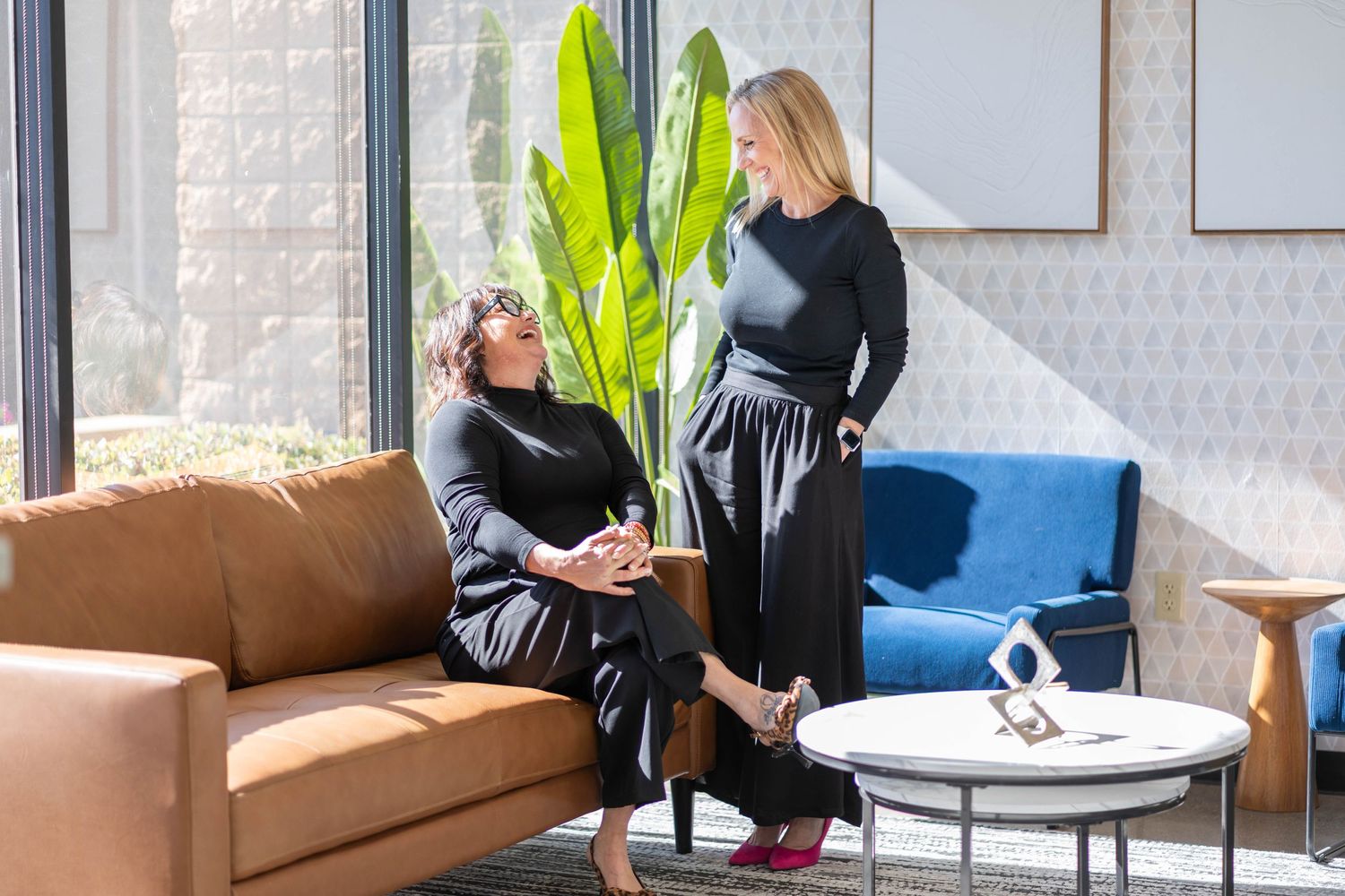women laughing together in an office with a brown chair, coffee table